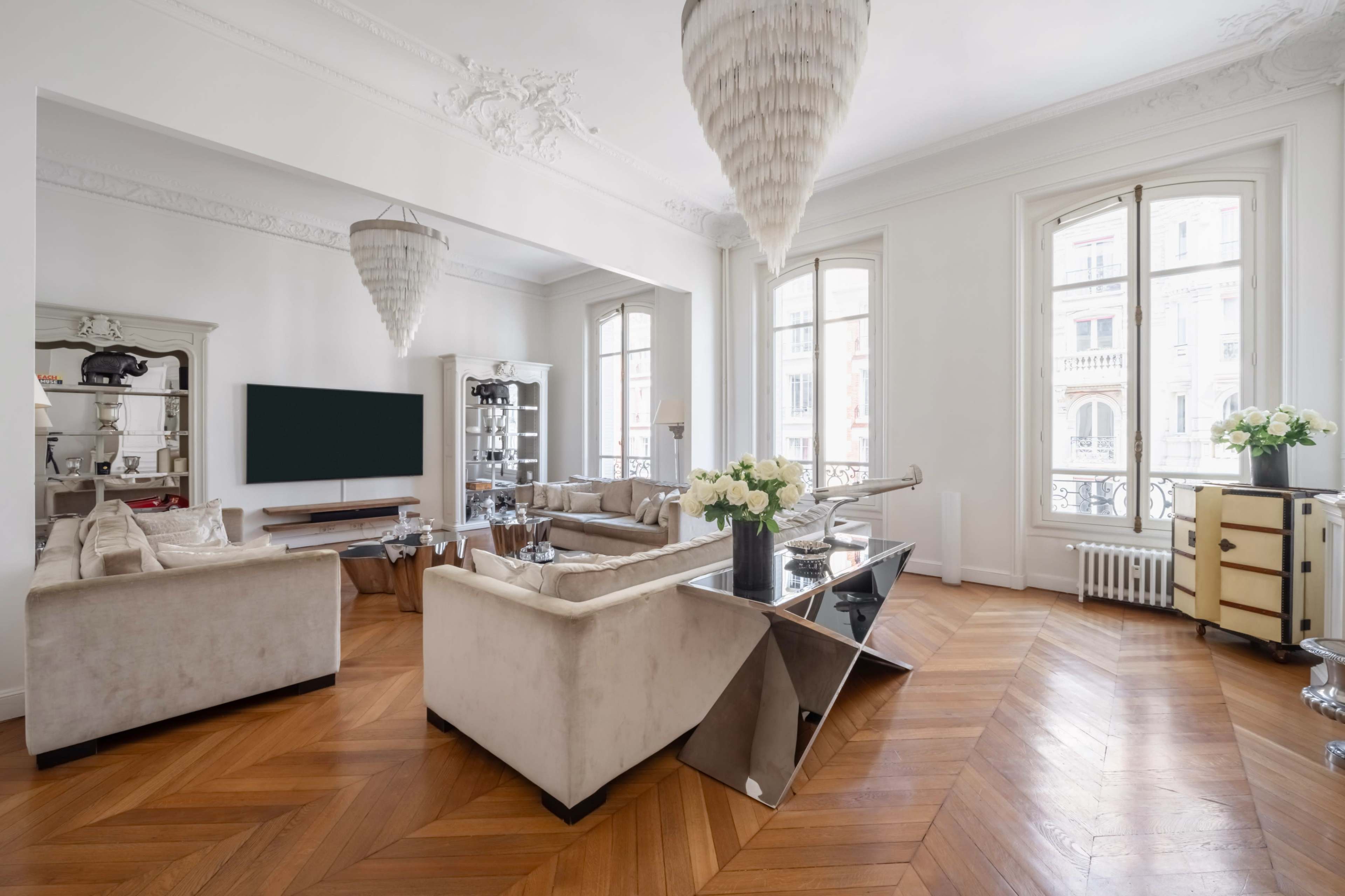 The image shows a stylish living room with hardwood flooring, modern furniture, and large windows allowing natural light to fill the space.