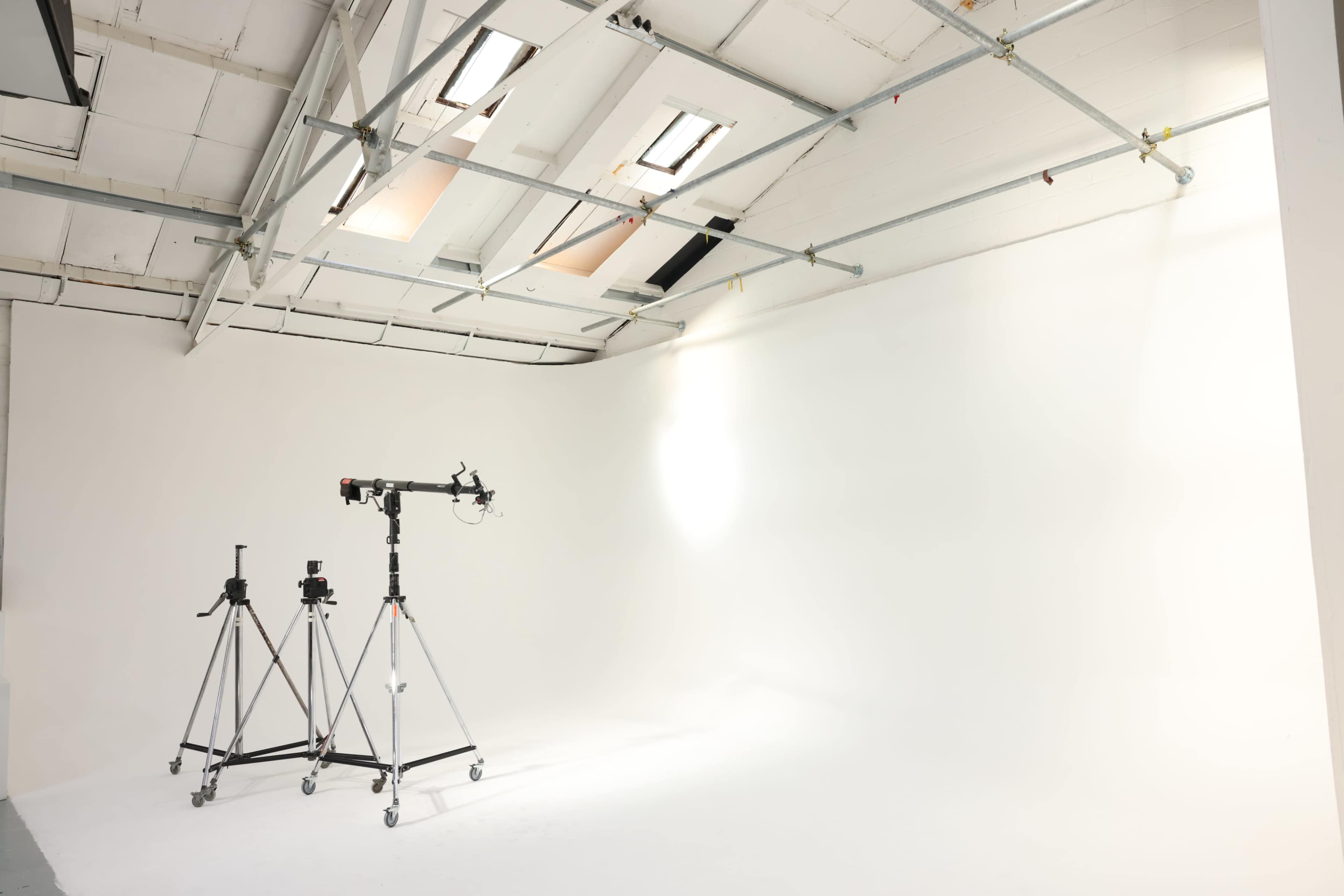 The image shows a bright, empty photo studio with two camera tripods positioned on a clean, white background.