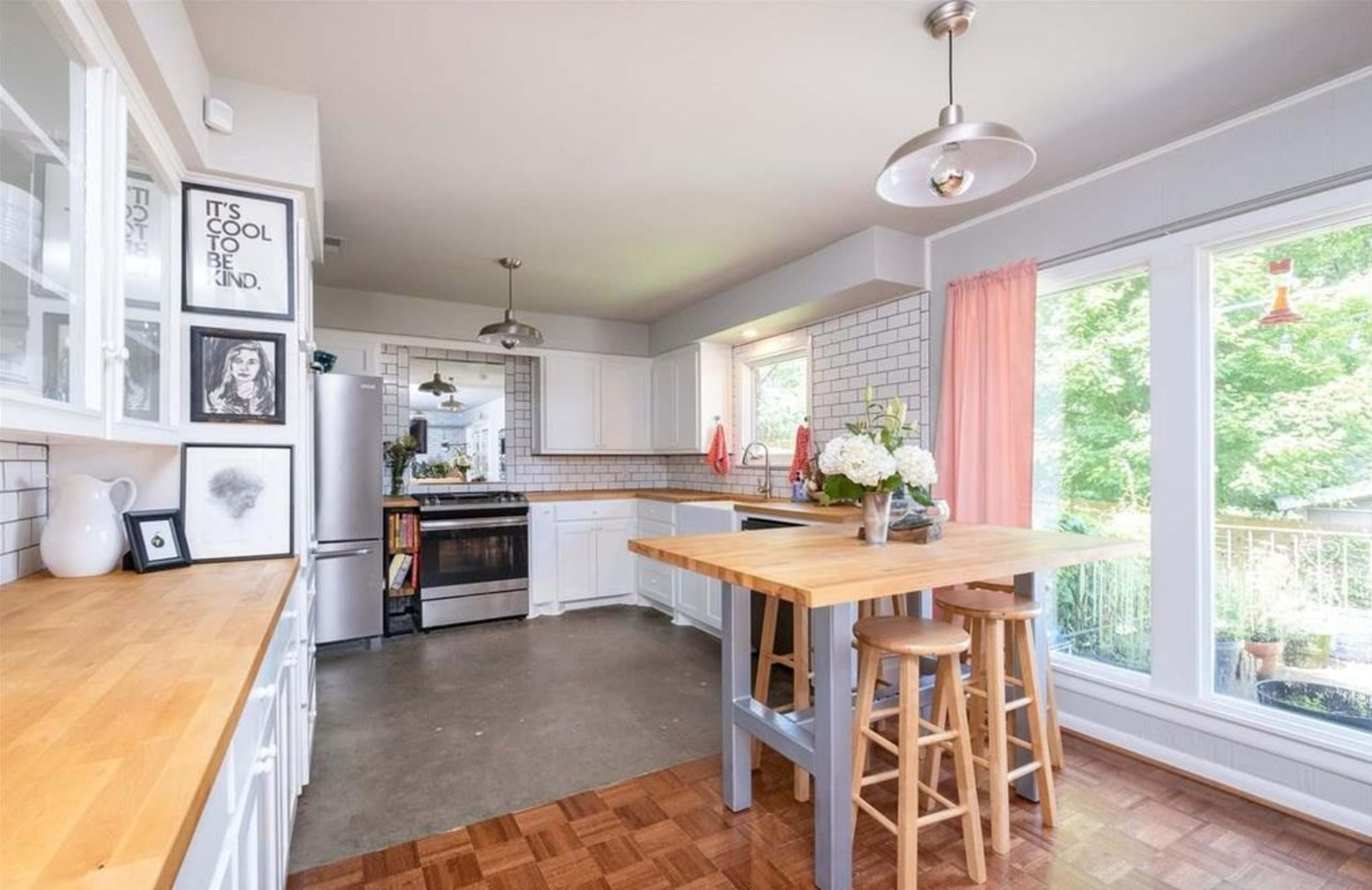 The kitchen features a large wooden table, stainless steel appliances, and white cabinets with a tiled backsplash.