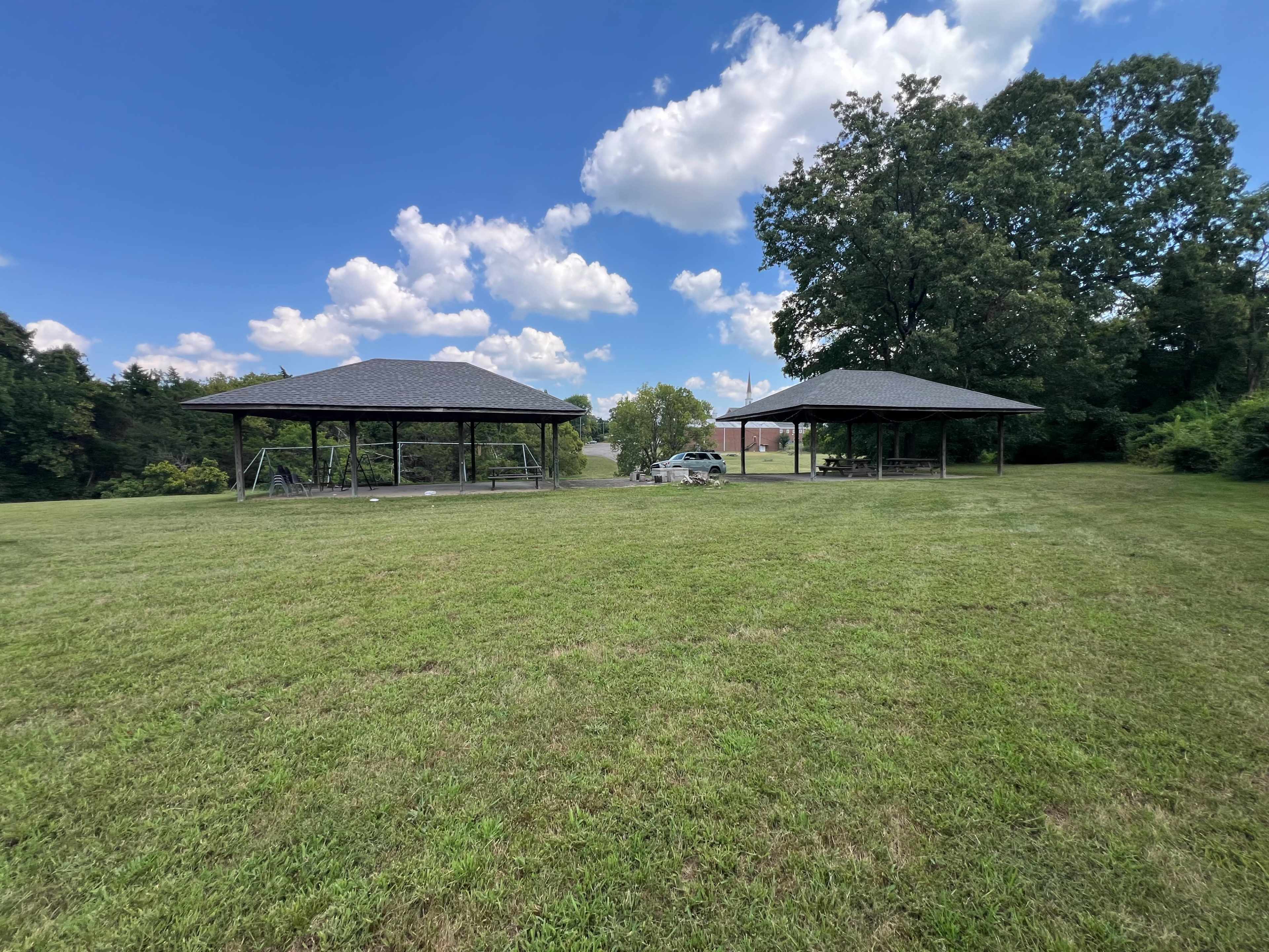 The image shows two pavilions in a grassy area under a blue sky with scattered clouds.