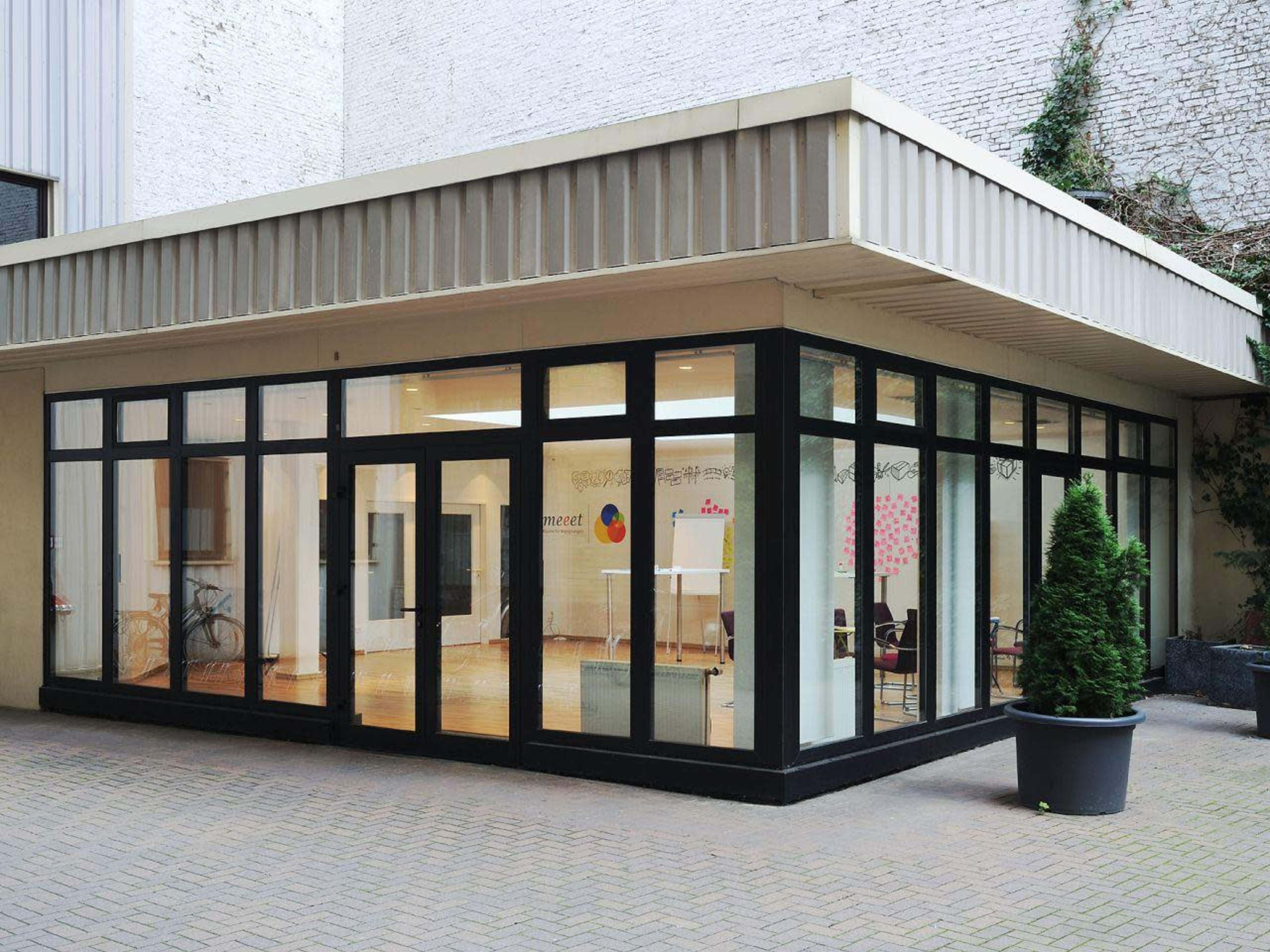 A modern glass-walled building with a minimalist design surrounded by a brick courtyard.