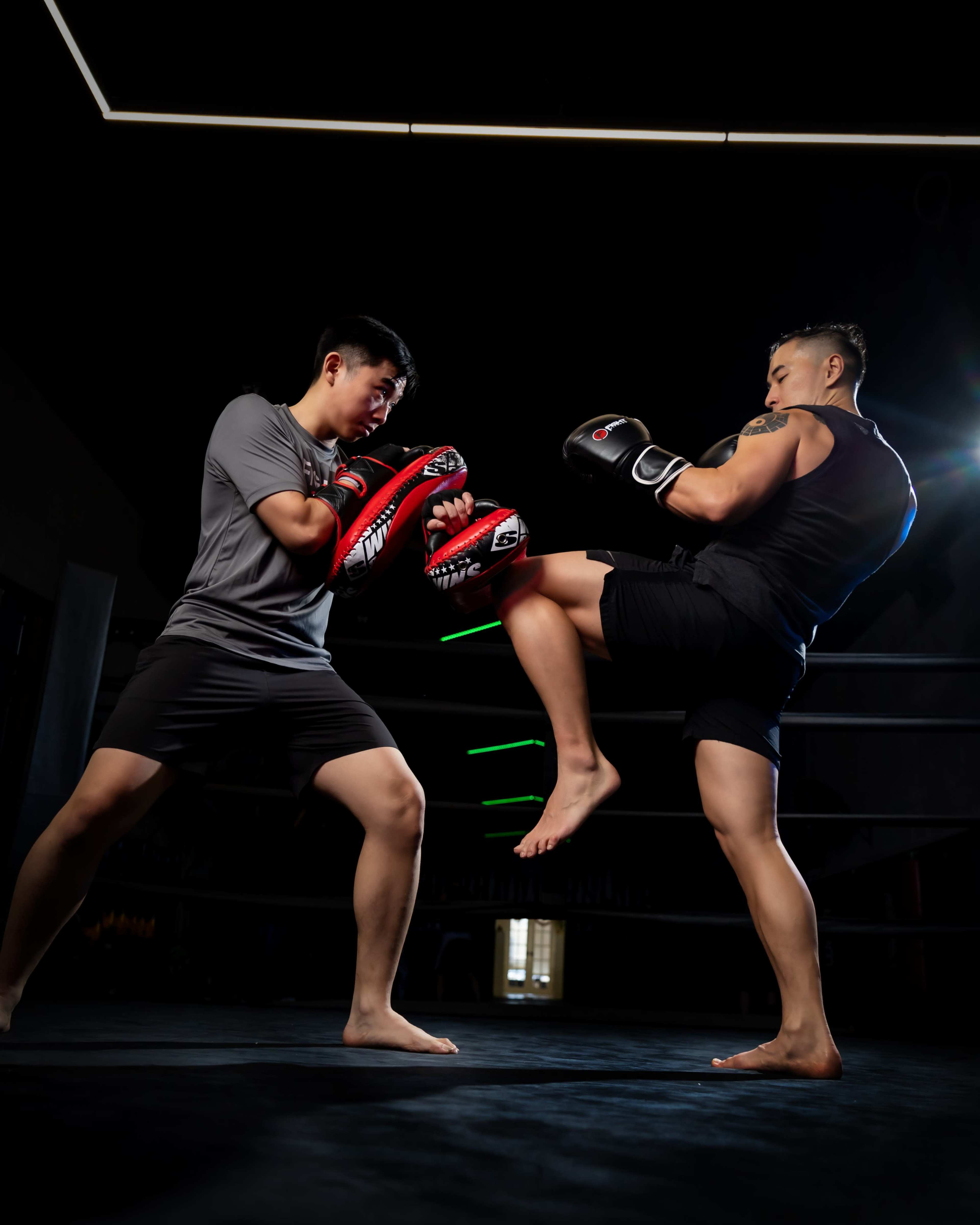 Two fighters engage in a sparring match in a dimly lit boxing ring.
