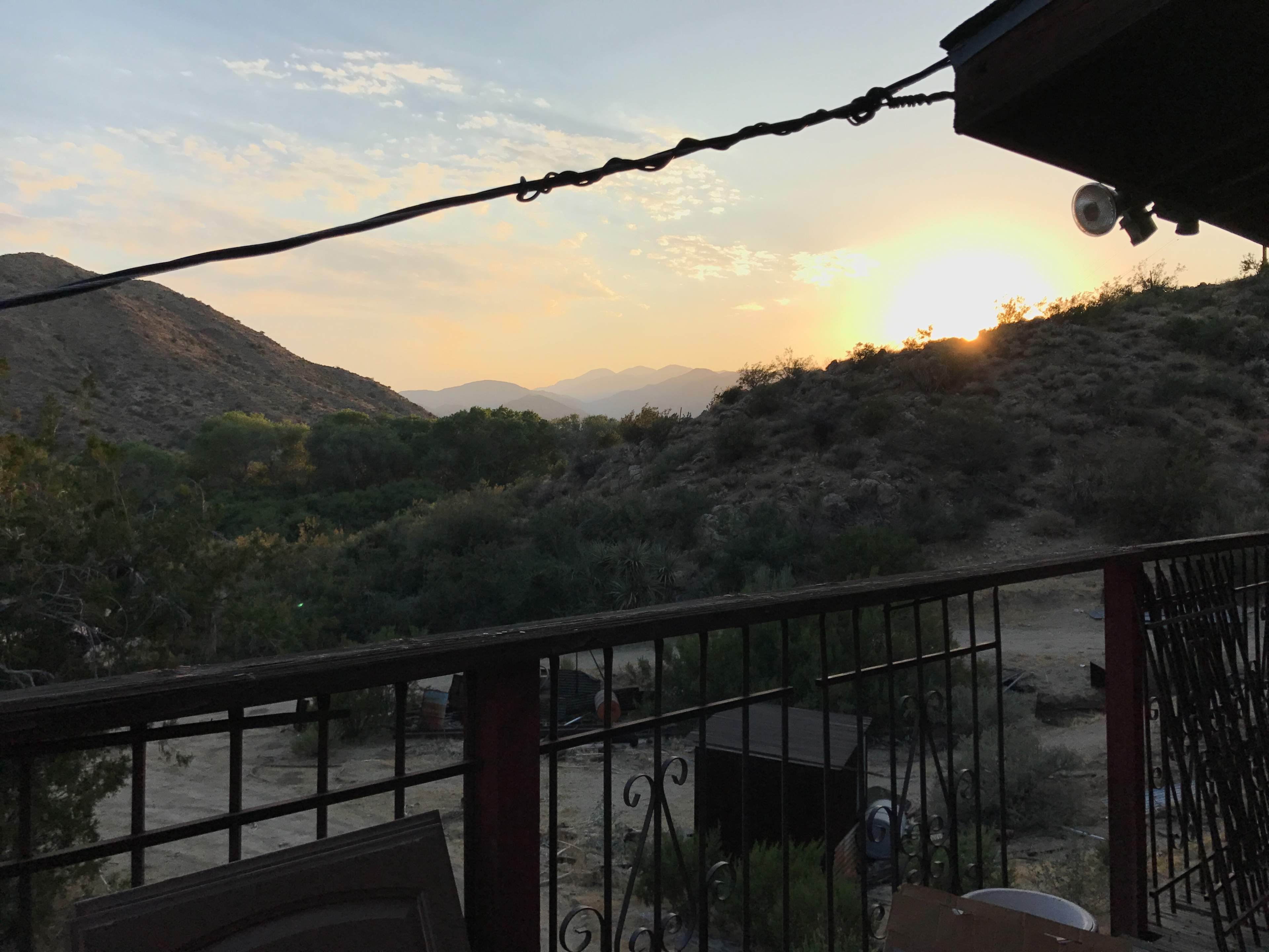 A mountainous landscape at sunset, viewed from a balcony with a railing.