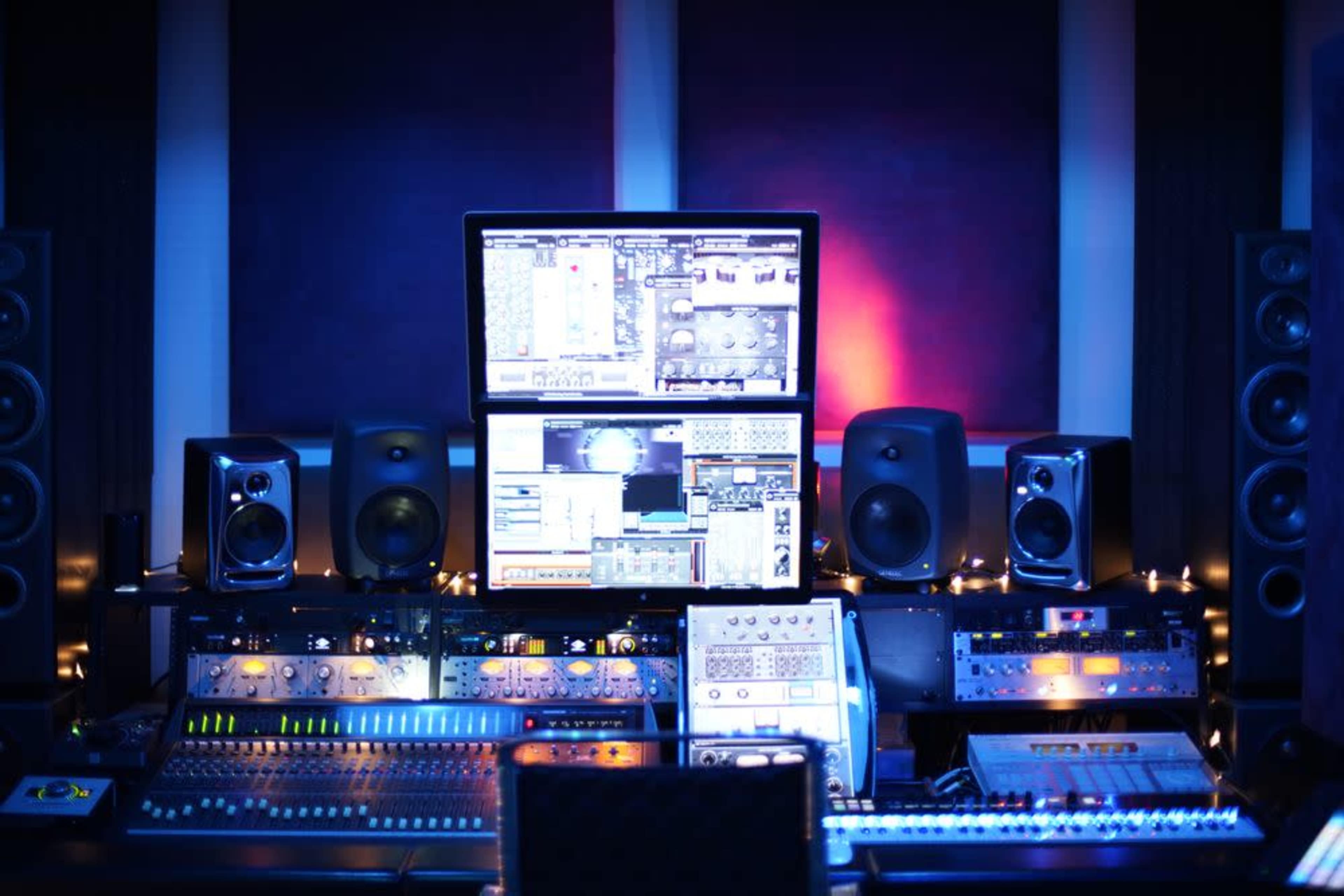 A music studio is filled with various audio equipment, featuring a large computer monitor displaying sound mixing software and multiple speakers.