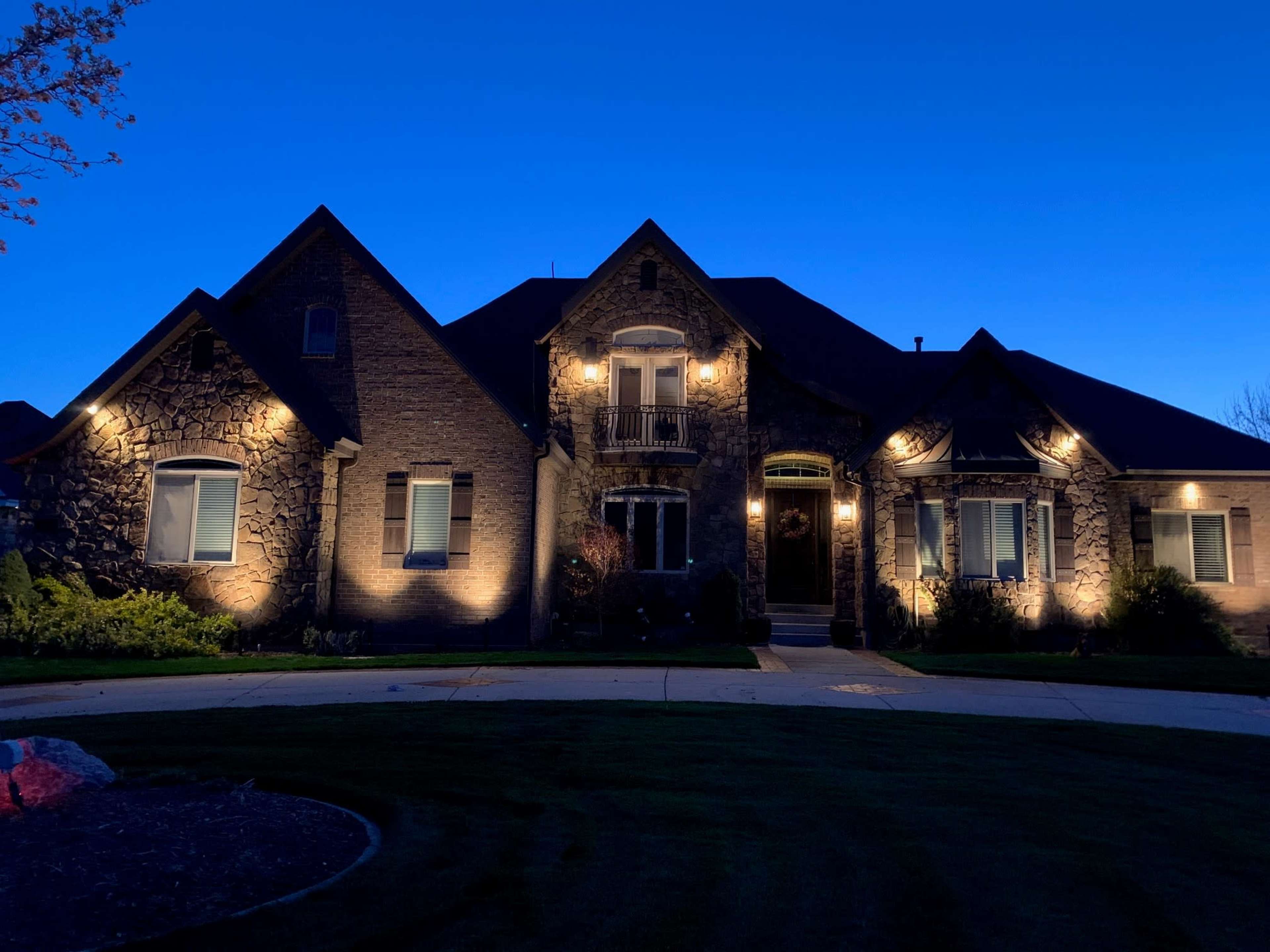 A large stone house is illuminated at dusk, showcasing its architectural features.