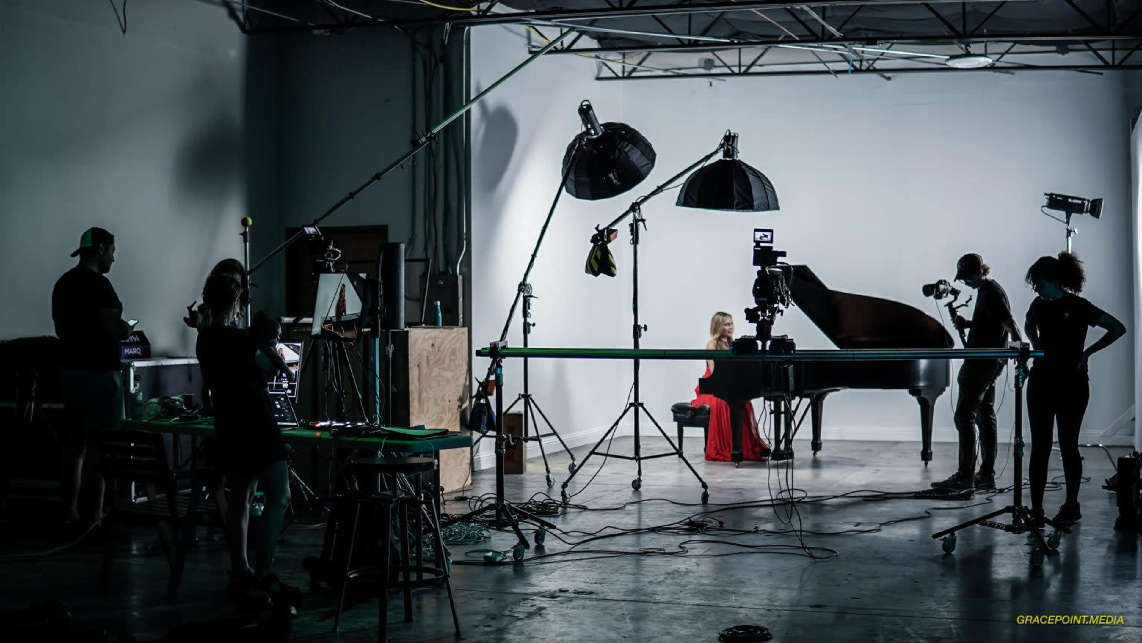 A photographer captures a musician playing a grand piano in a studio setup with multiple lights and cameras.