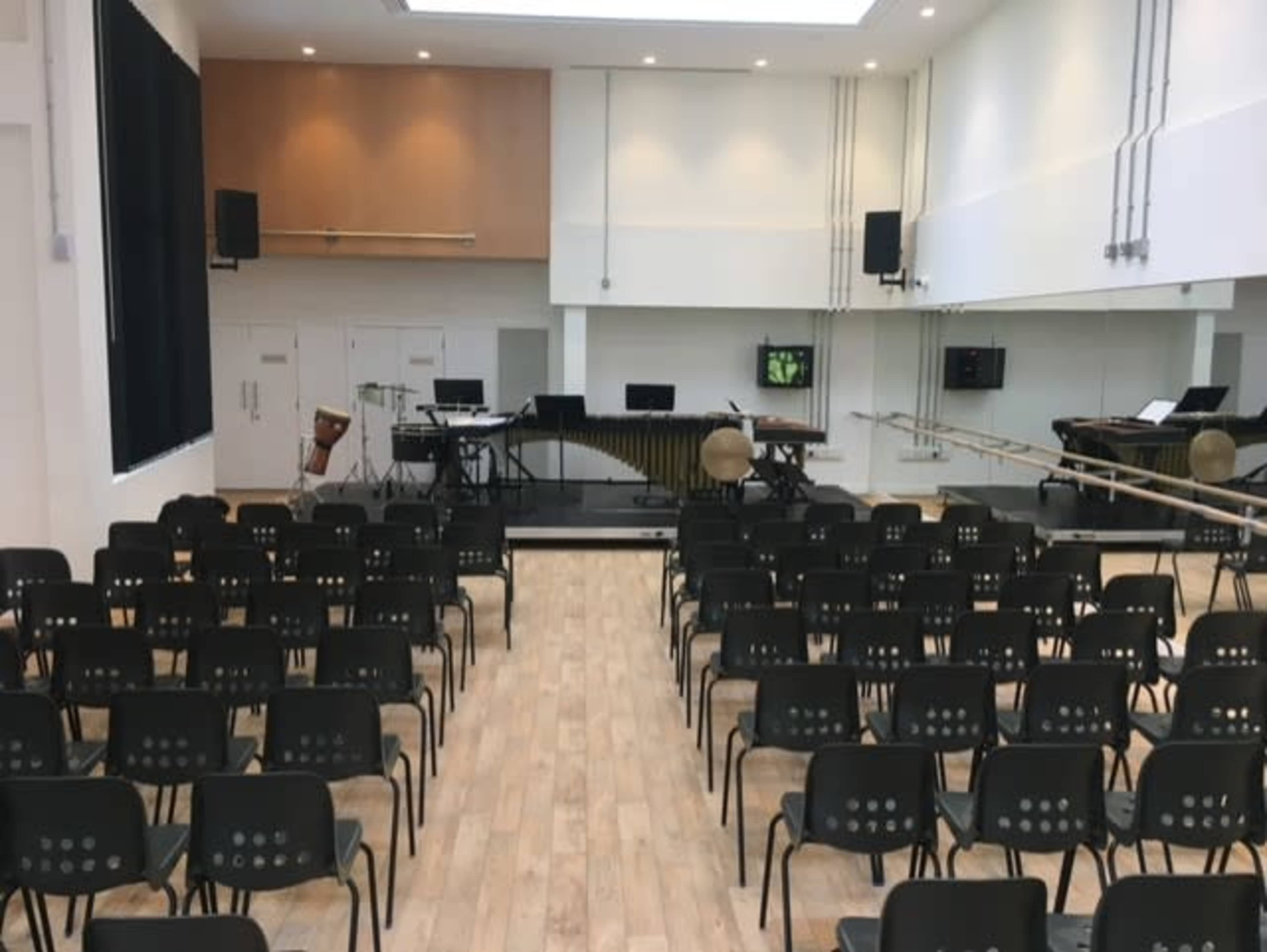 A music performance space with rows of black chairs facing a stage equipped with various musical instruments.