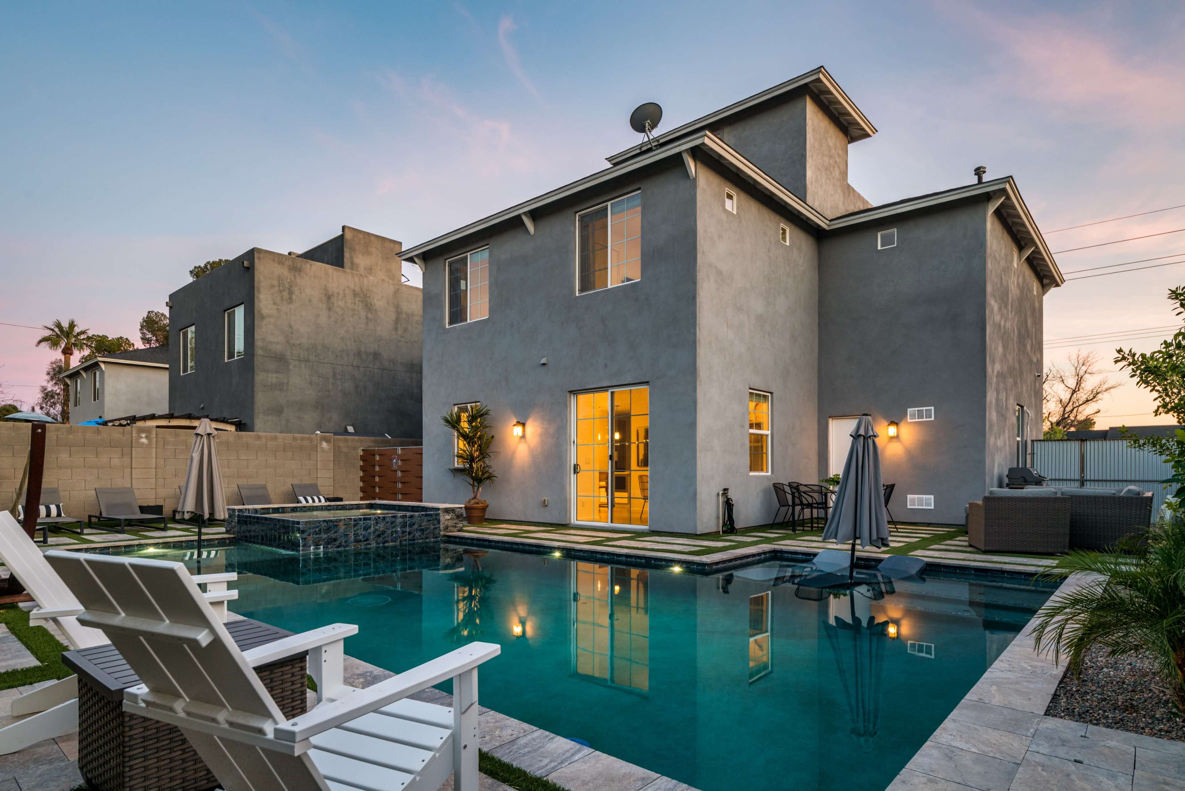 The image shows a modern two-story house with a pool and outdoor seating area in the backyard.