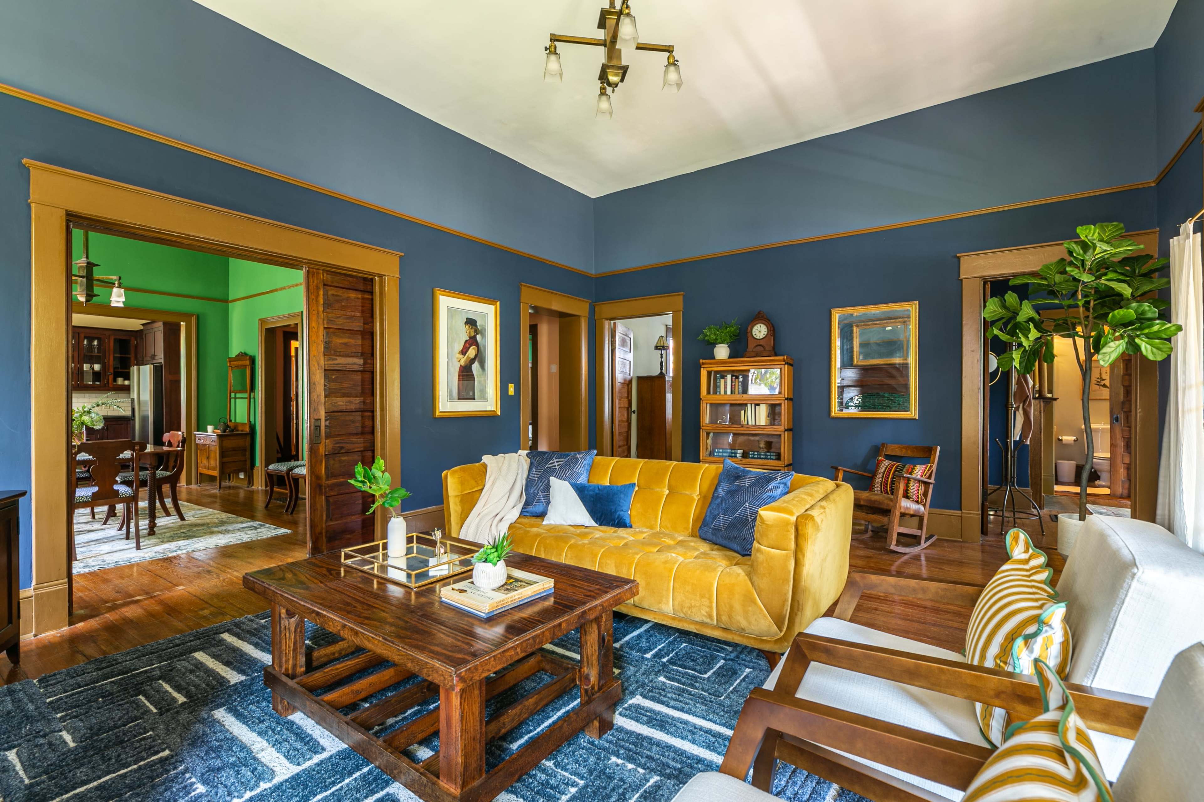 A living room with a yellow sofa, a wooden coffee table, and a blue wall, showcasing doorways leading to adjacent rooms.