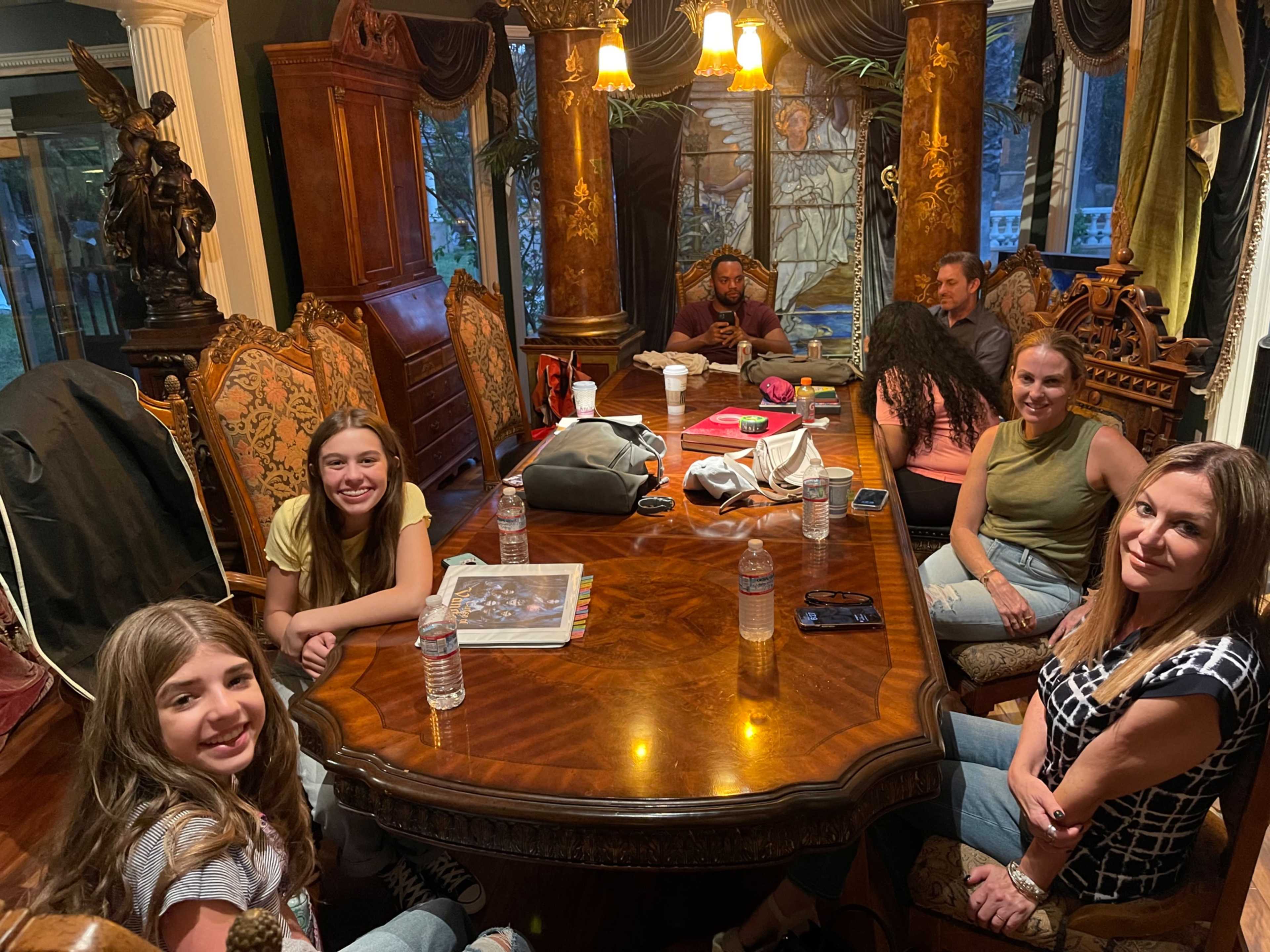A group of people is seated around a large, ornate dining table in a well-decorated room.
