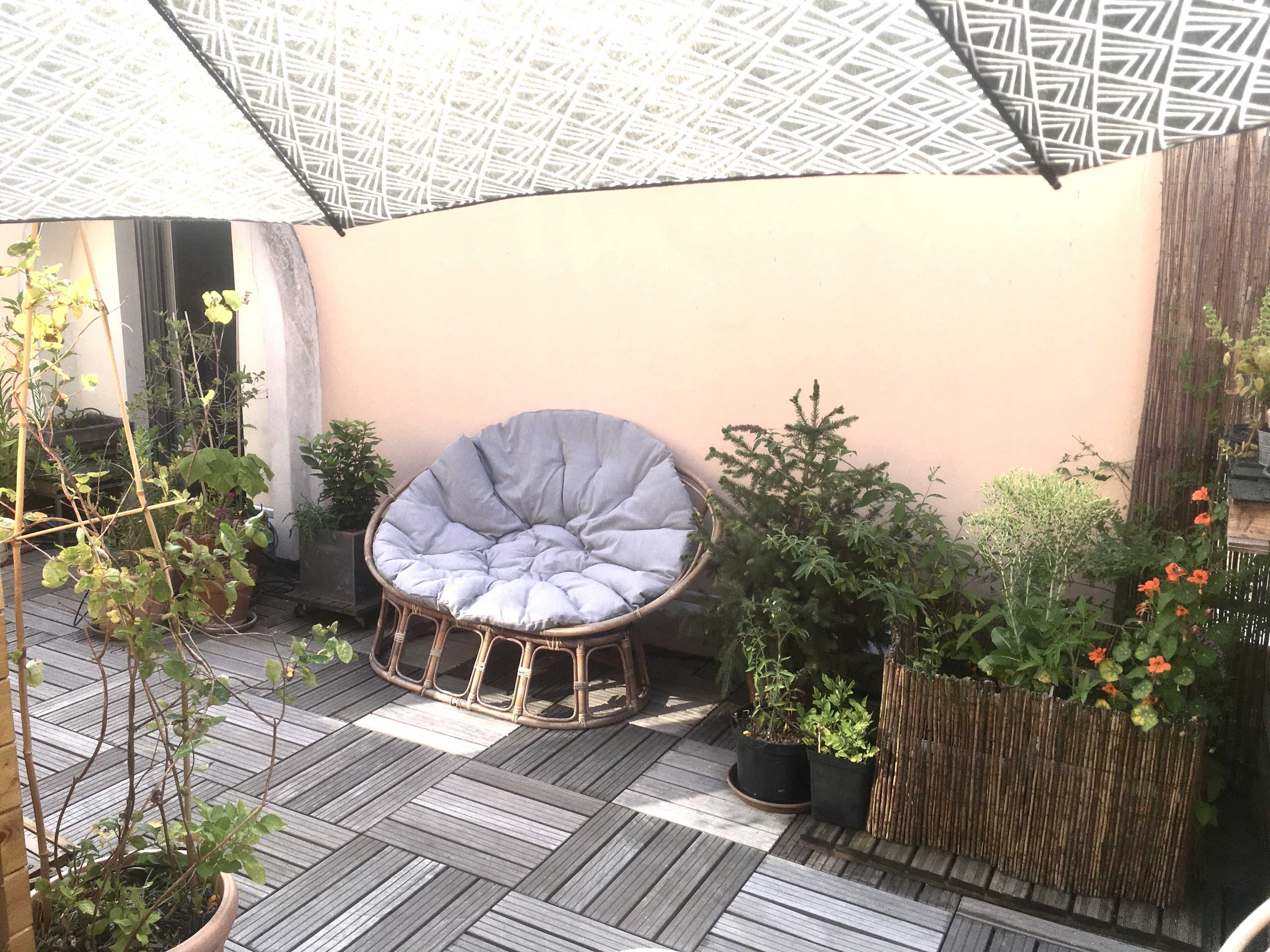 A patio with a round cushioned chair surrounded by various potted plants and a patterned canopy overhead.