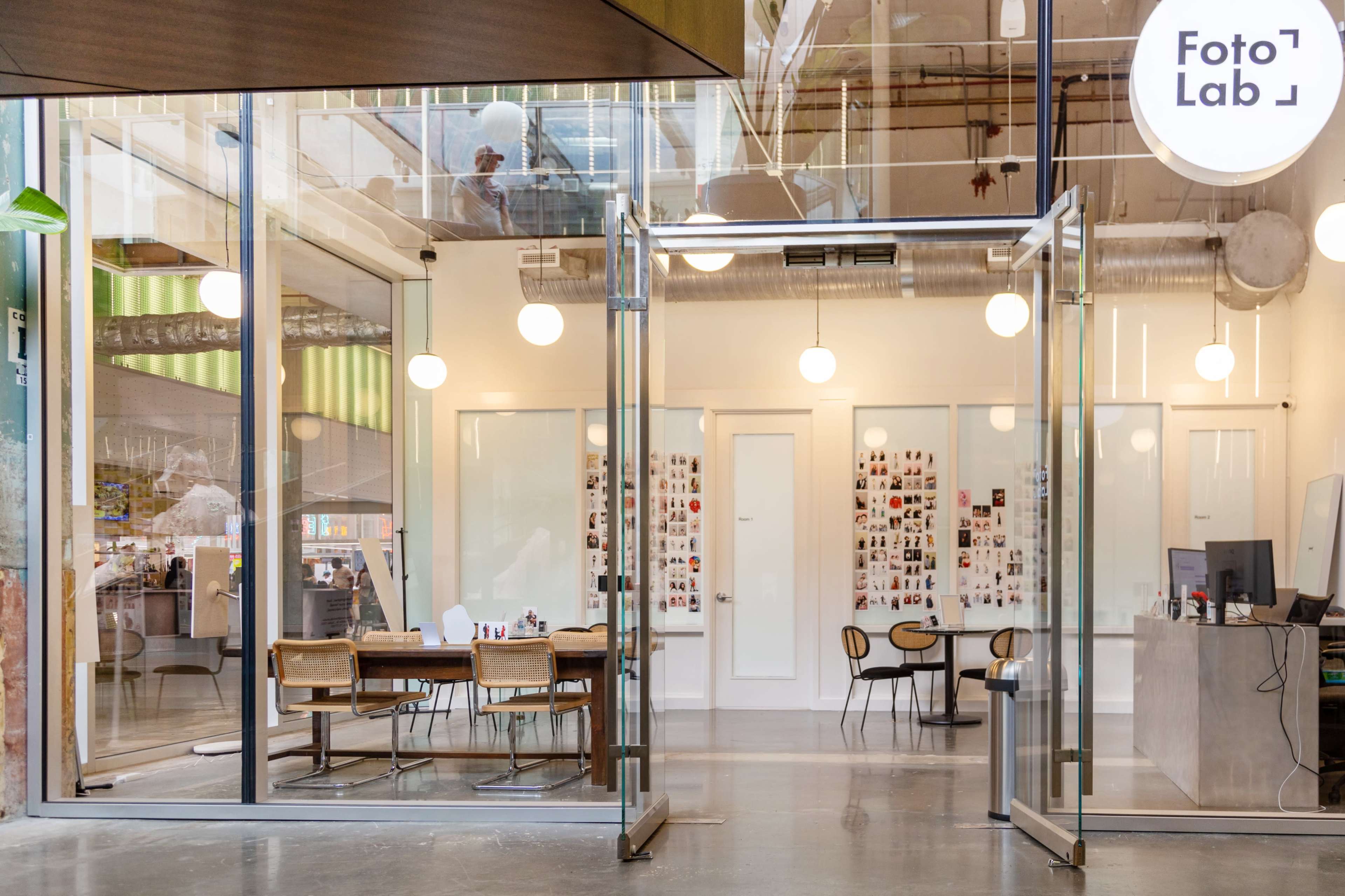 The entrance of a modern photo lab with large glass doors, displaying a bright interior that includes tables and a counter.