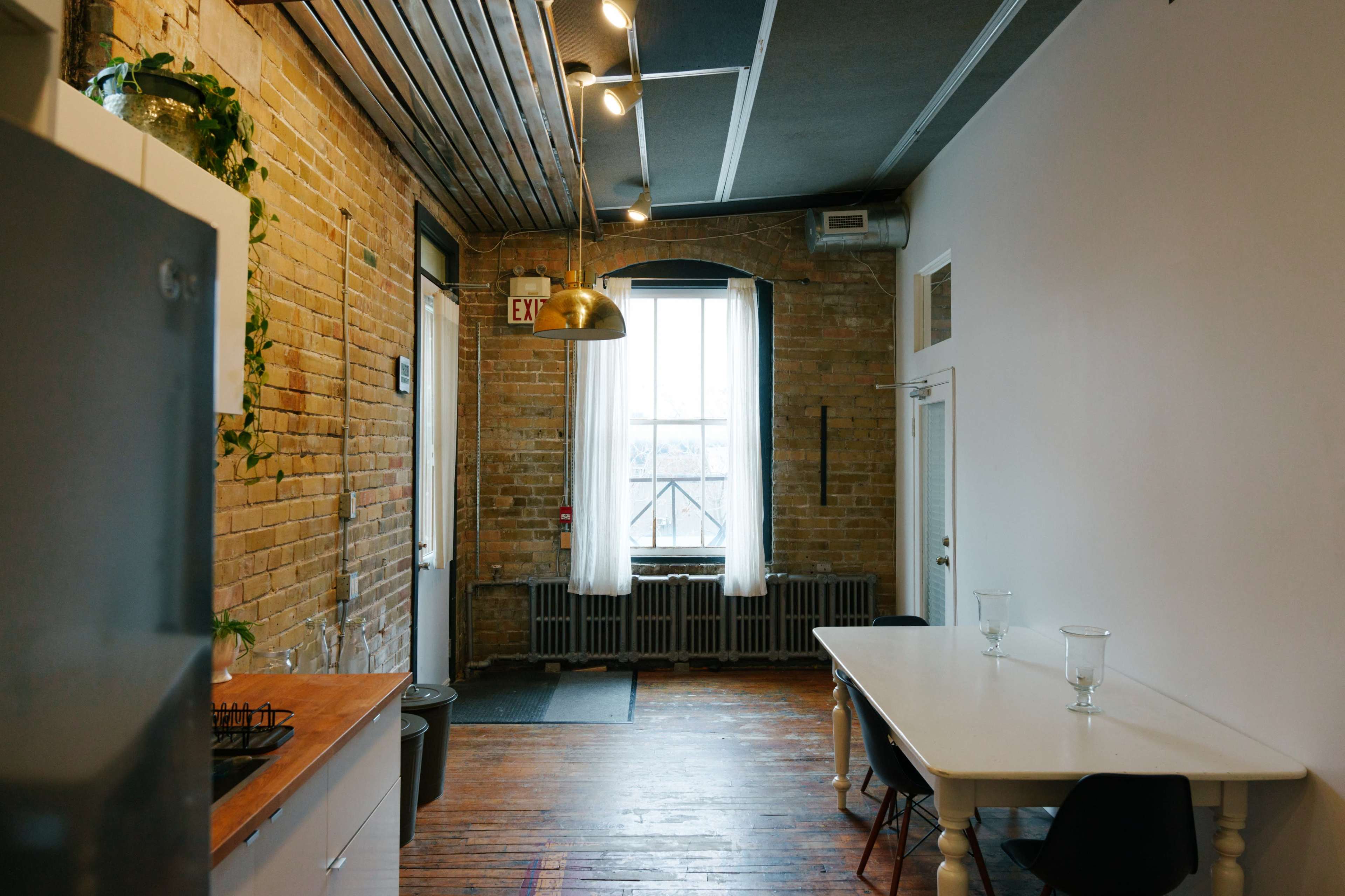 A spacious kitchen and dining area featuring exposed brick walls, wooden floors, and a large window with natural light.