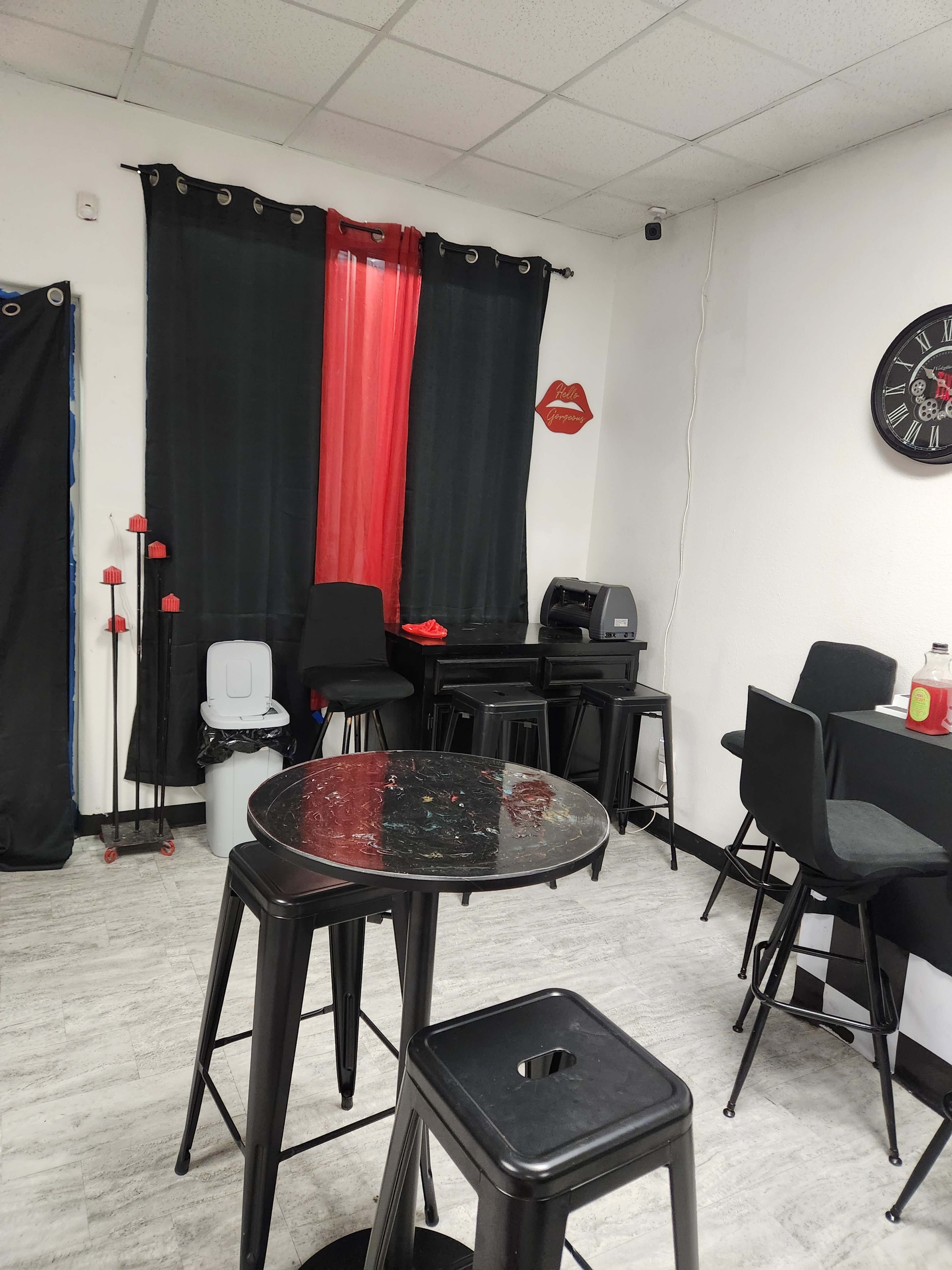 The image shows a small, modern room with black tables and chairs, red accents, and a clock on the wall.