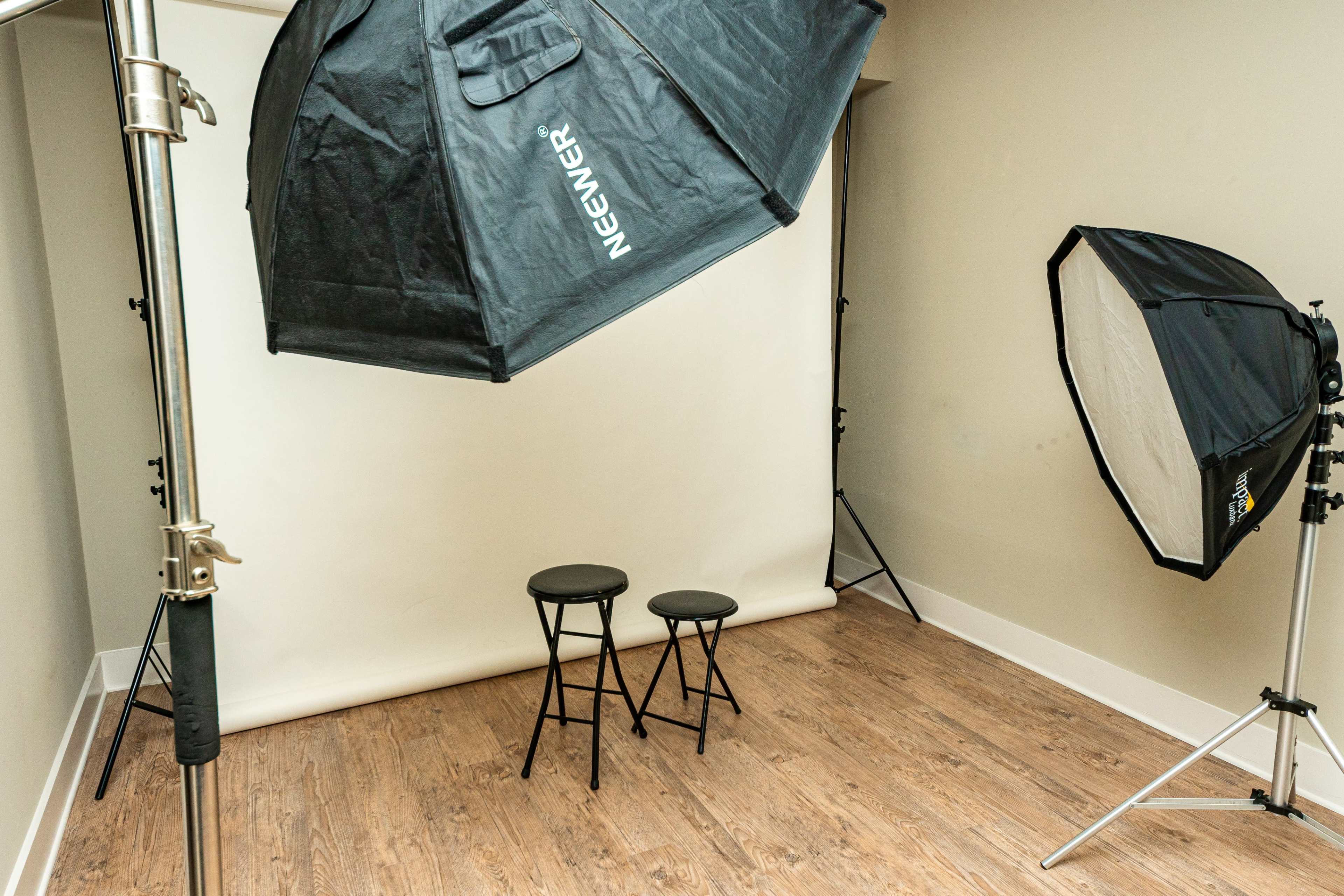 A photography studio features two black stools positioned in front of a seamless backdrop, with light softboxes set up on either side.
