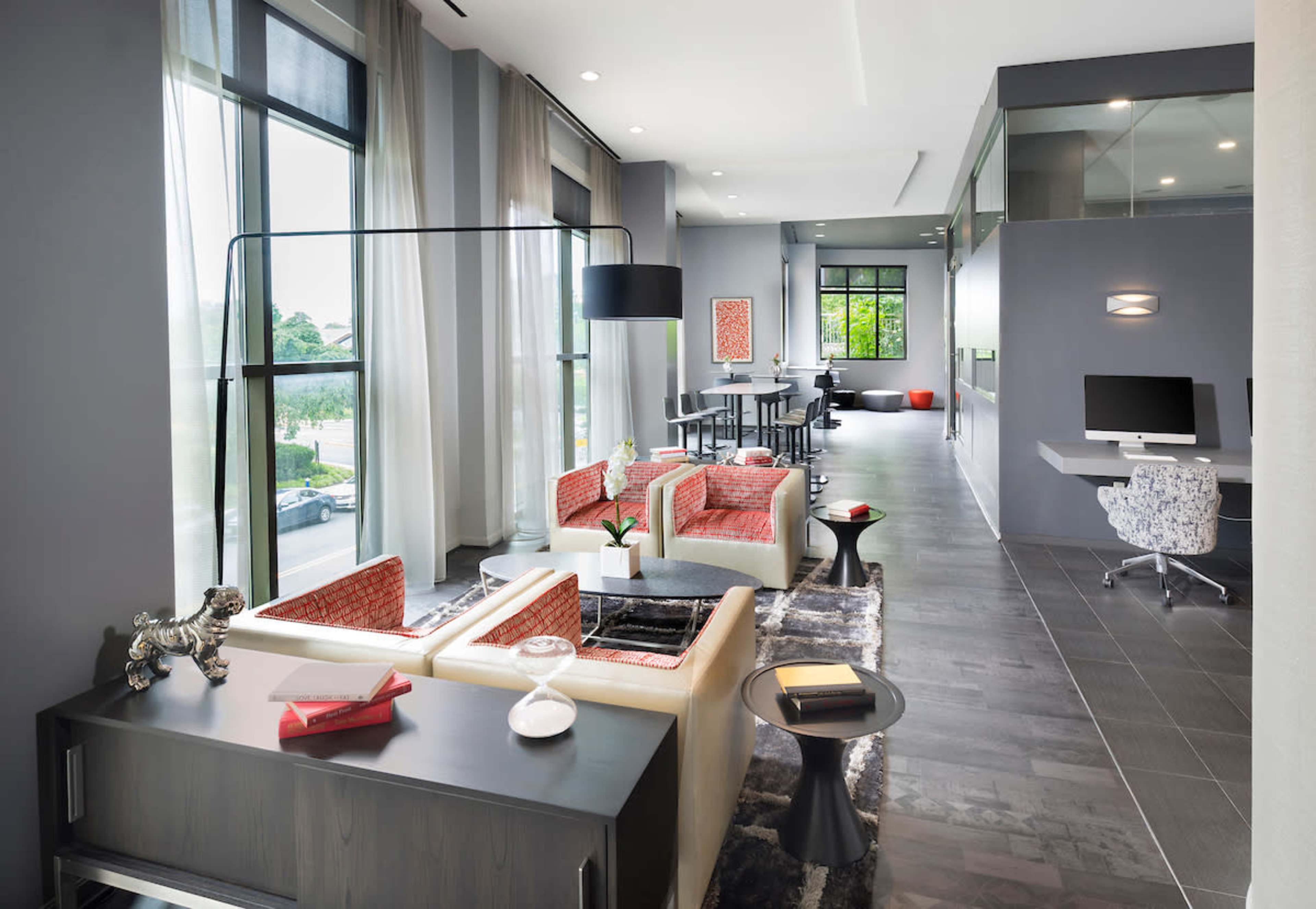 A modern living space with a comfortable seating area, a dining space, and a workstation, all featuring large windows that allow natural light to flood the room.