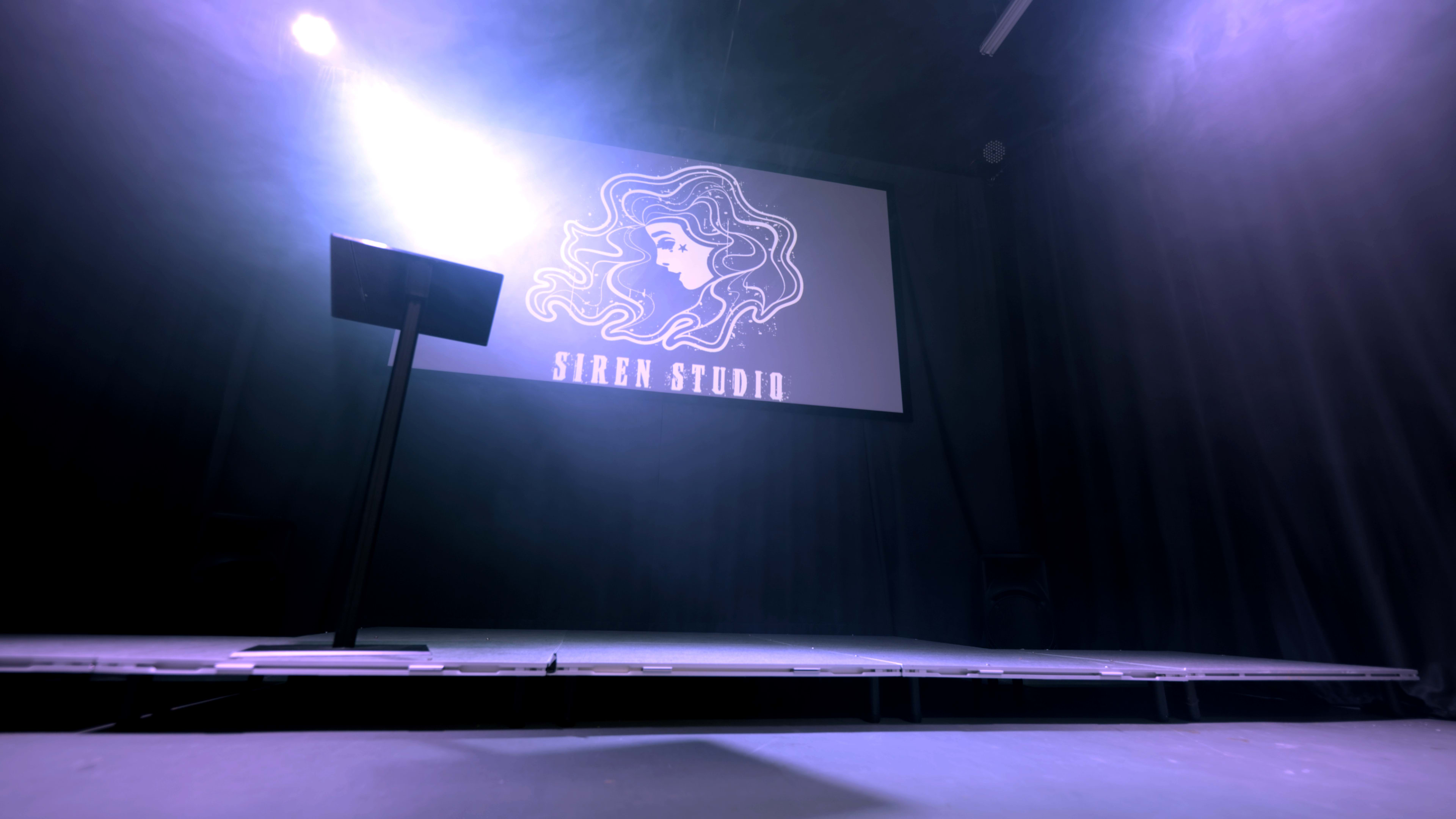 A stage with a podium, featuring a backdrop displaying the "Siren Studio" logo of a woman with flowing hair.
