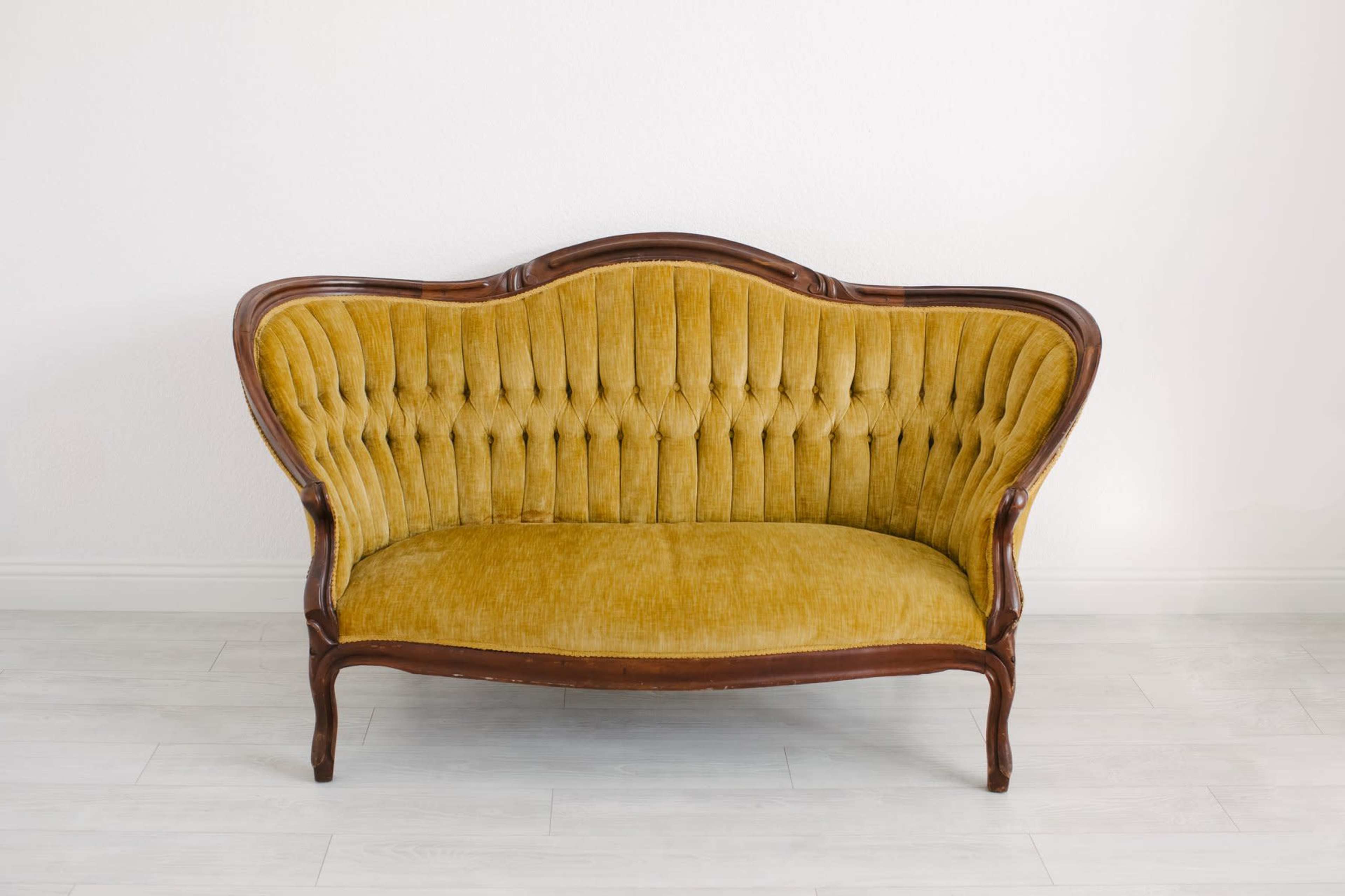 A vintage yellow tufted sofa with a wooden frame placed against a plain white wall.