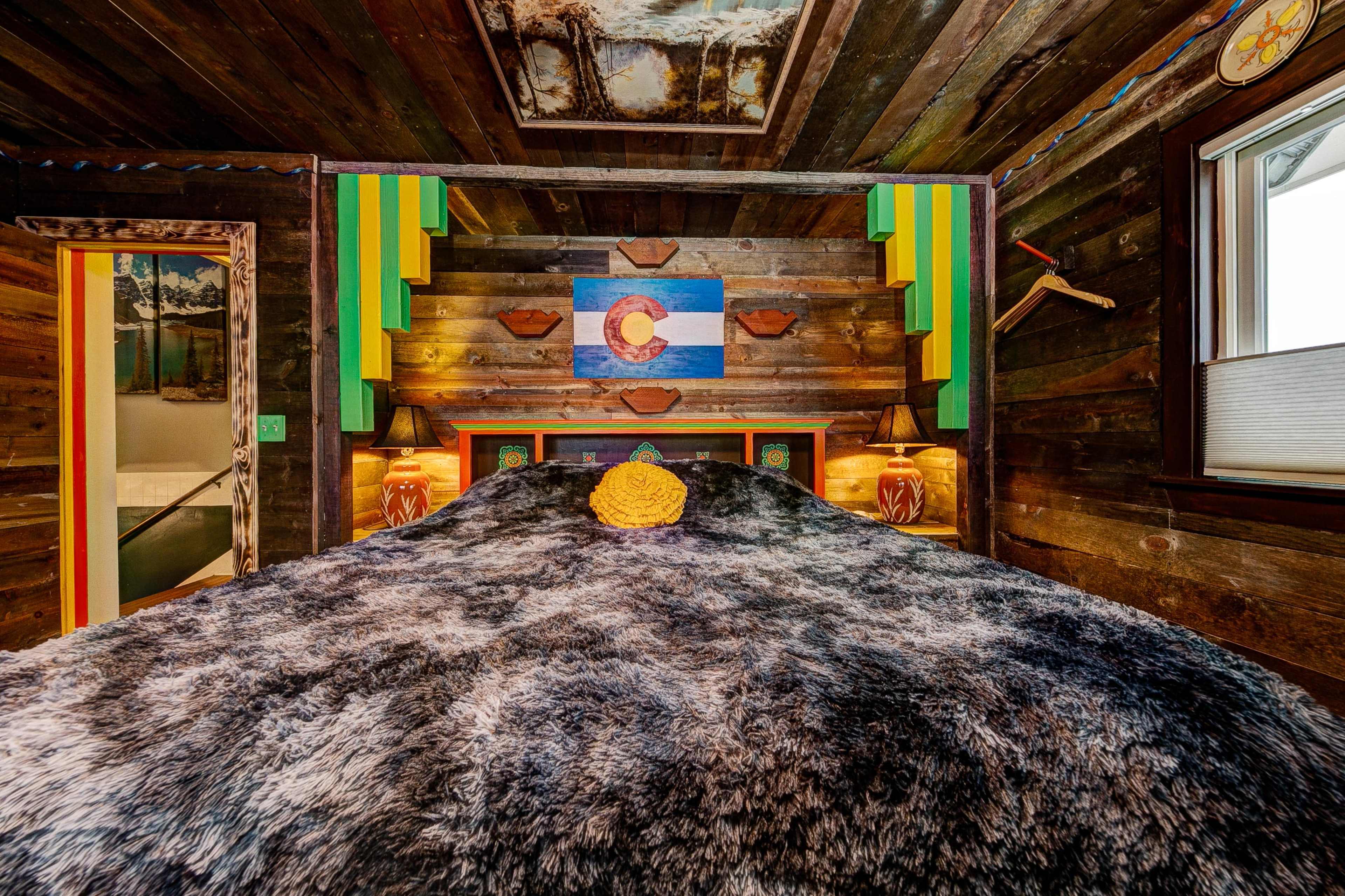A bedroom with a large, dark fur blanket on the bed, colorful wall decor featuring the Colorado flag, and wooden walls.