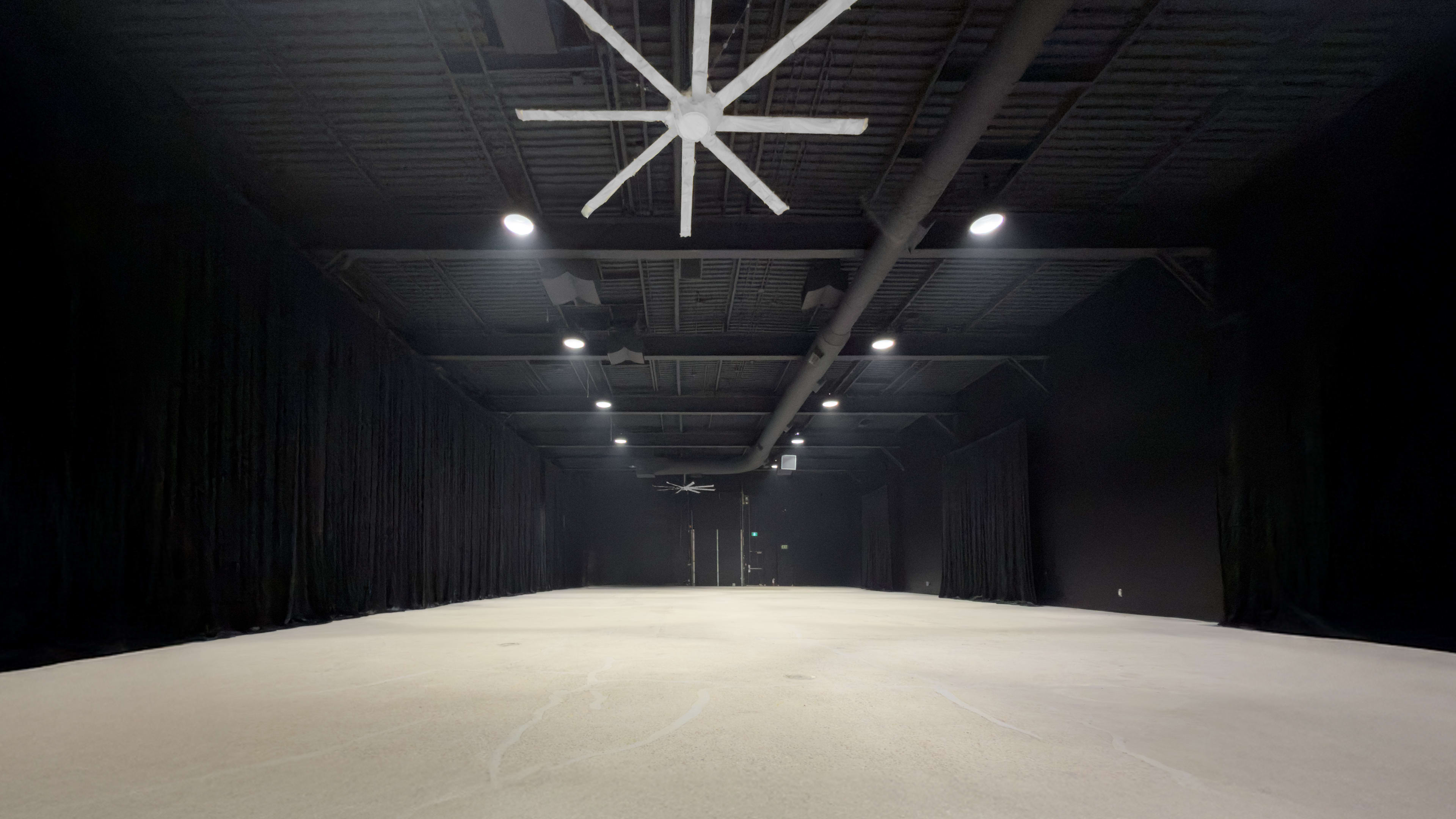 The image shows a spacious, dimly lit room with black curtains lining the walls and a light-colored carpeted floor.