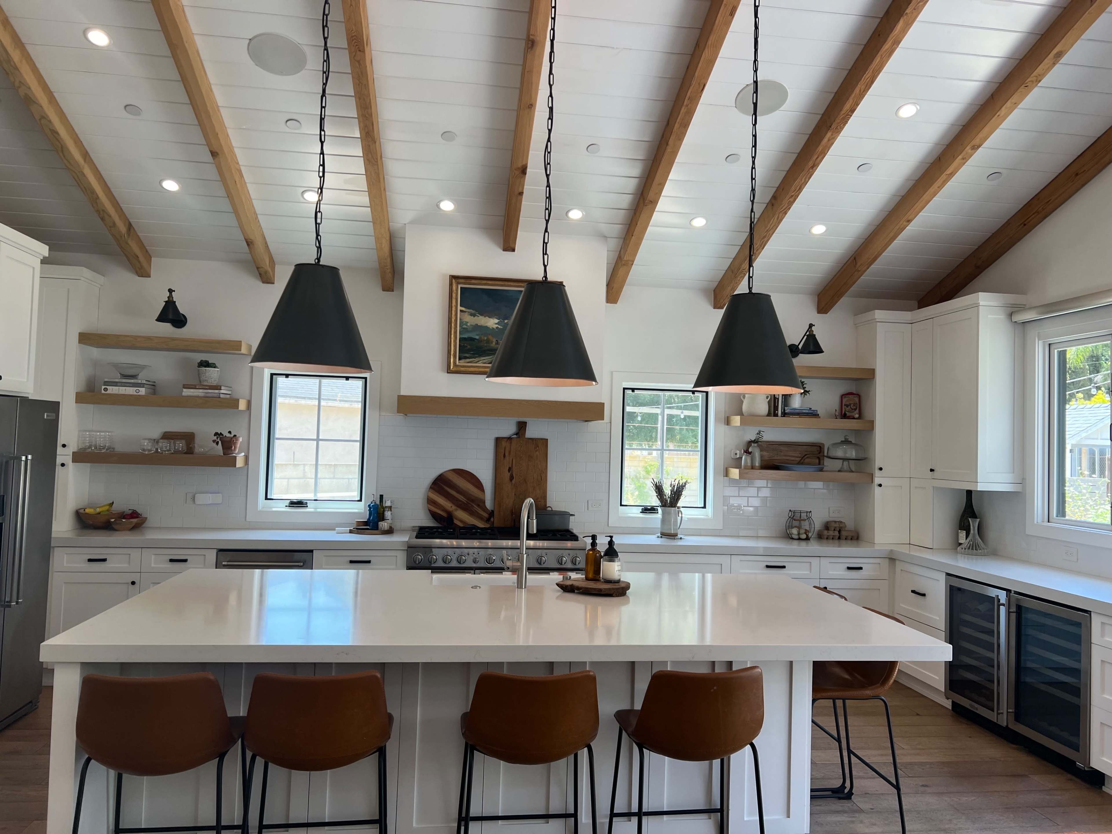 A modern kitchen with a large island, pendant lights, wooden beams on the ceiling, and stainless steel appliances.