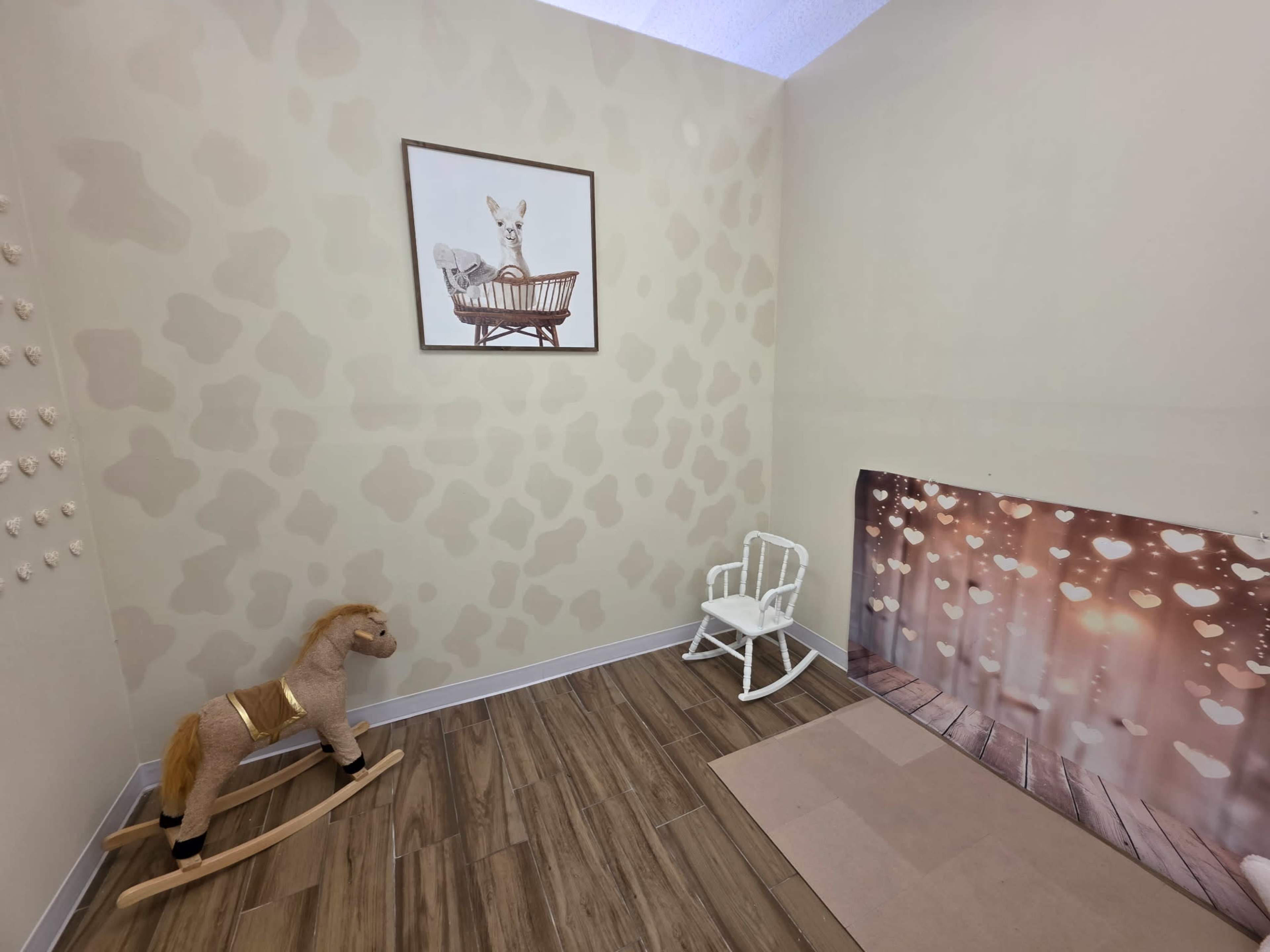The scene shows a small room with a decorated wall featuring a framed picture, a rocking horse, a white wooden chair, and a section of patterned flooring.