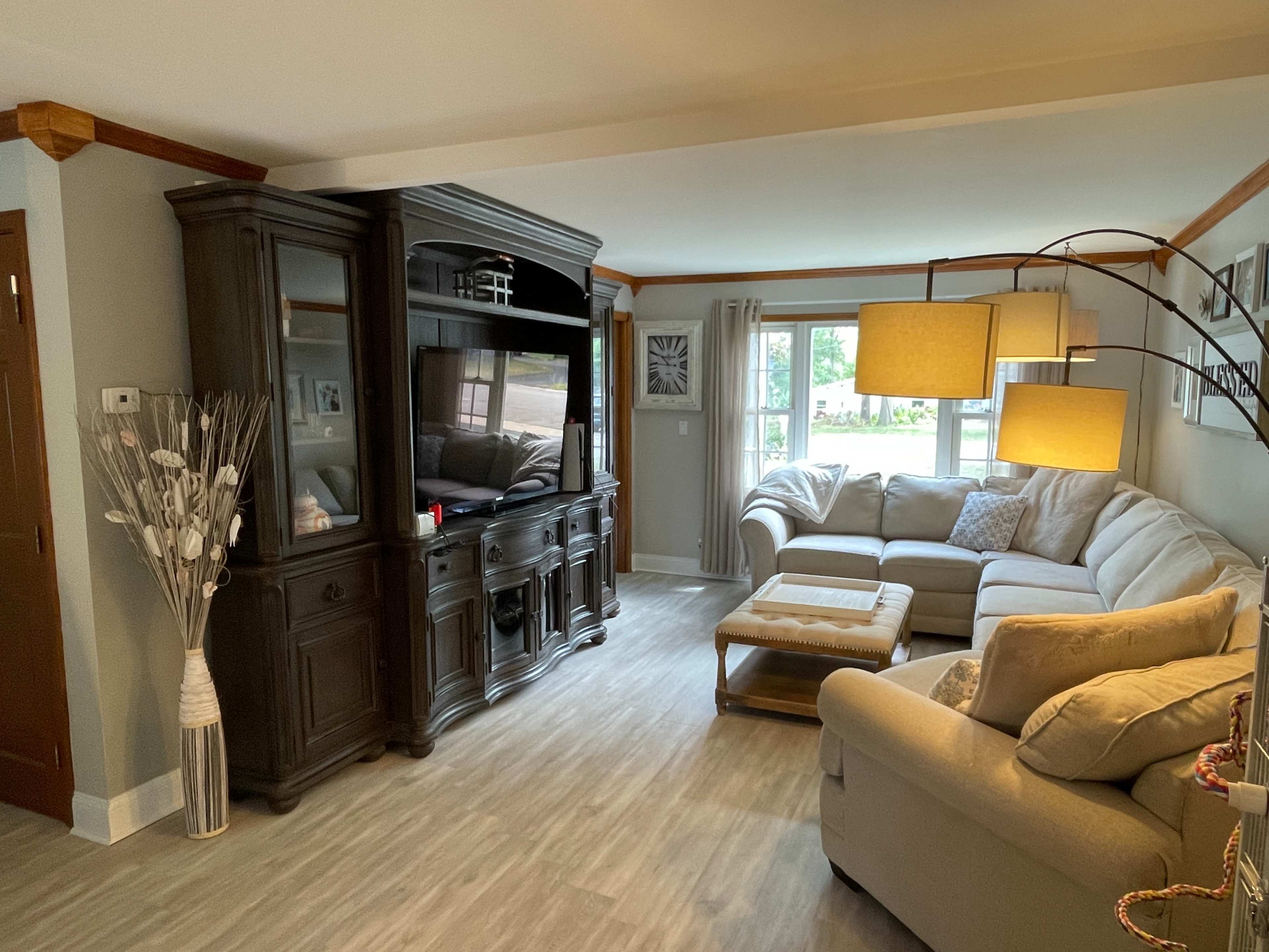 The image shows a living room with a large sectional sofa, a coffee table, a TV cabinet, and a floor lamp.