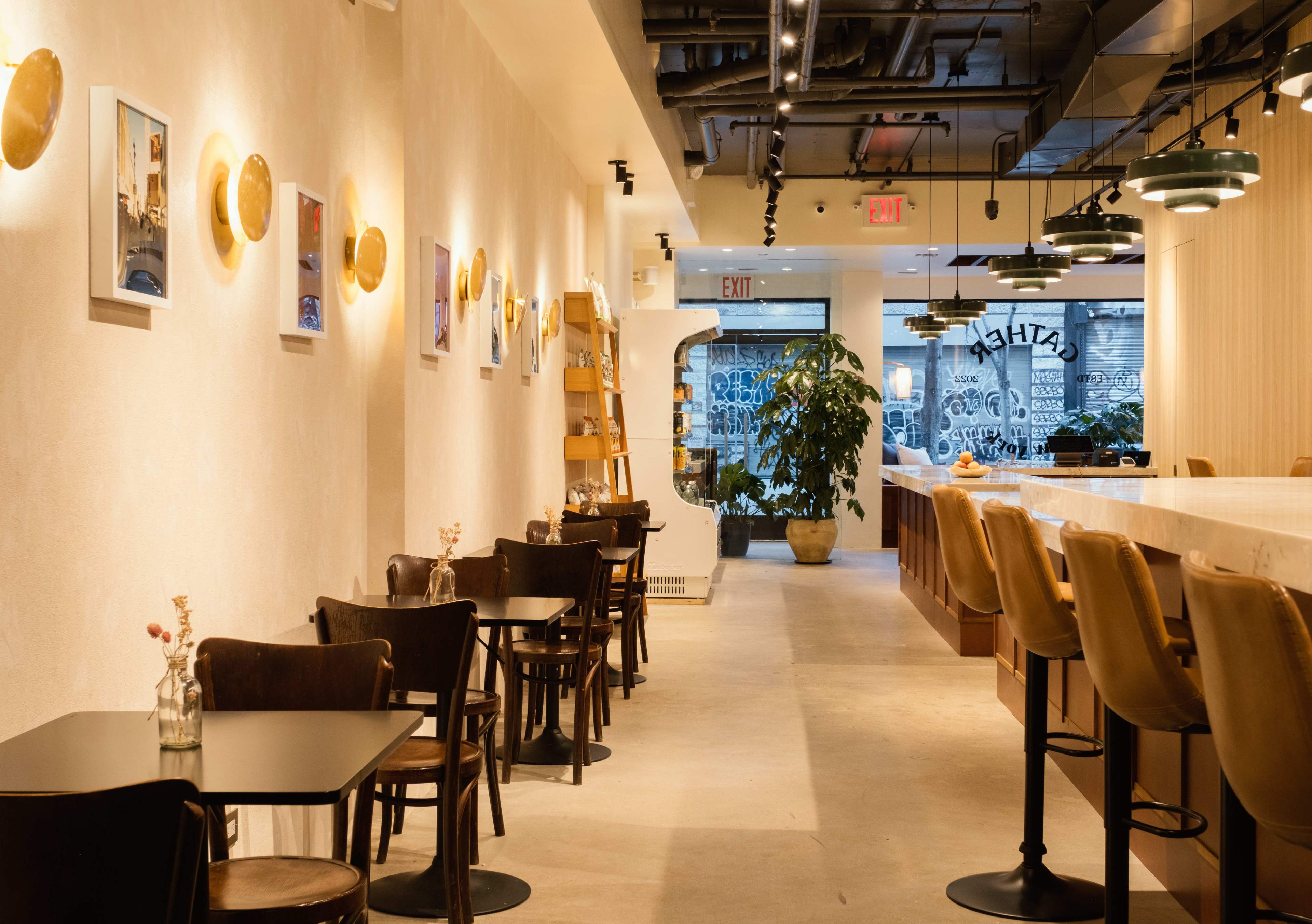 A modern café interior with tables and chairs along one side and a large bar area with backlit shelves on the other.