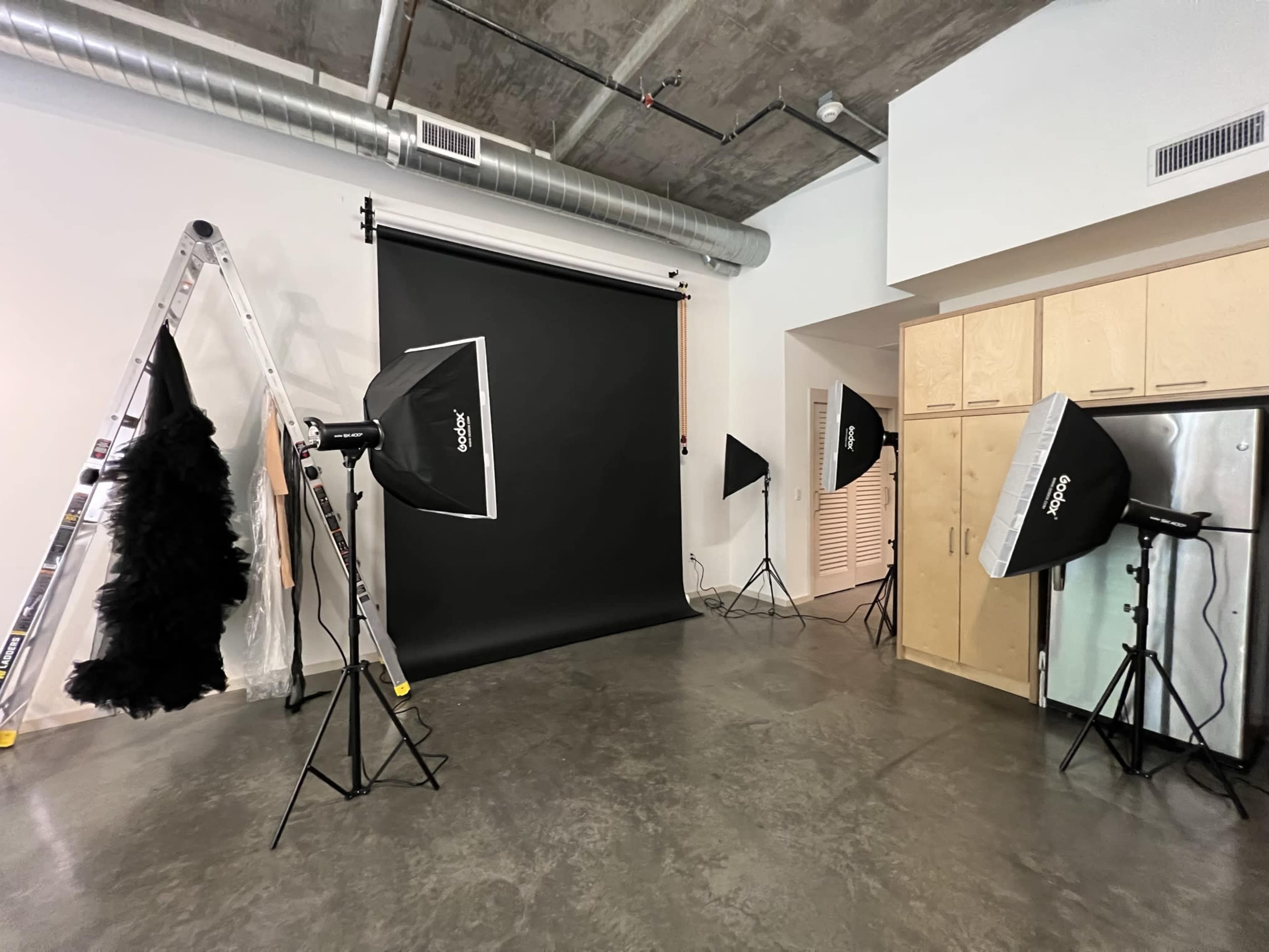 A photography studio with a black backdrop, several lighting setups, a ladder, and a garment rack displaying a costume.