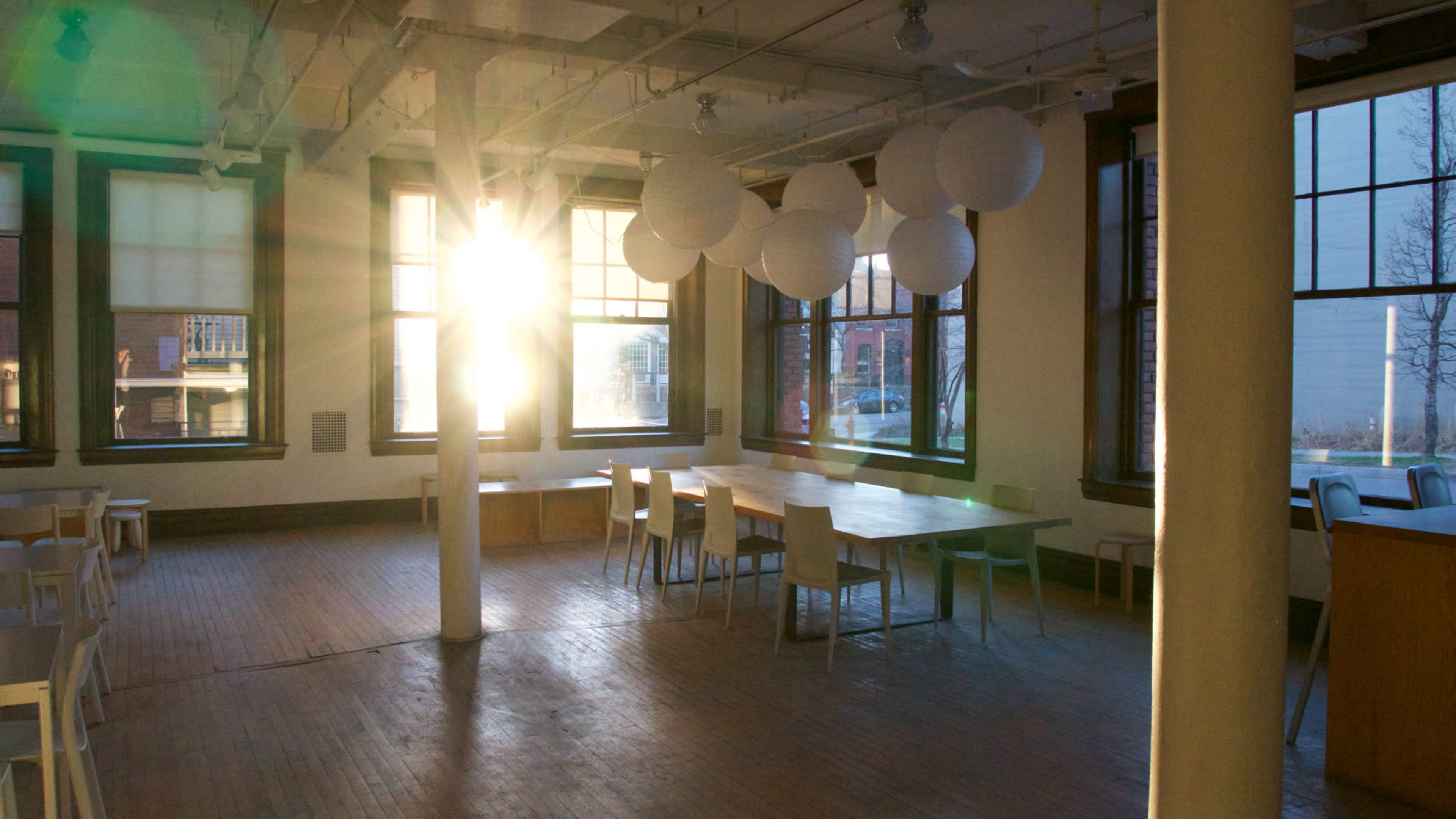 A sunbeam streams through large windows, illuminating a spacious room with wooden floors and simple white furniture.