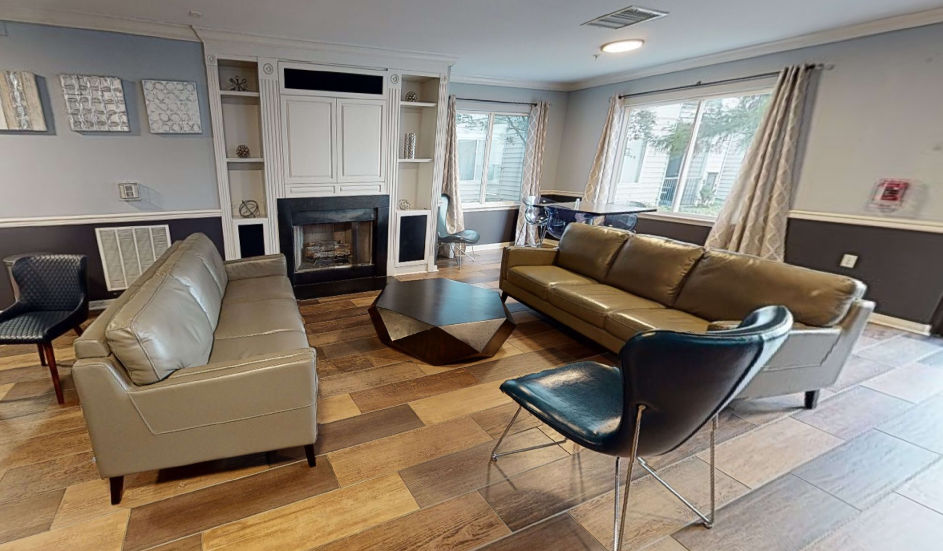 A living room with two sofas, a coffee table, and a fireplace, surrounded by windows and a blue chair.