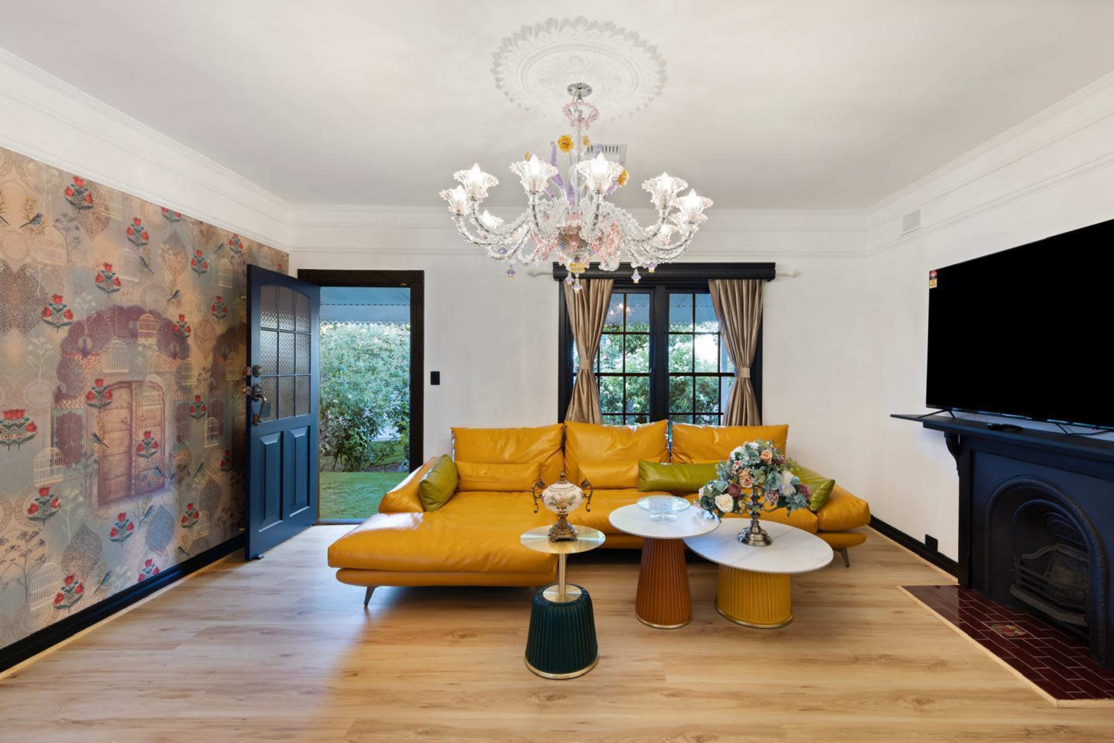 The living room features a yellow sectional sofa, a chandelier, two coffee tables, and a wall adorned with patterned wallpaper.