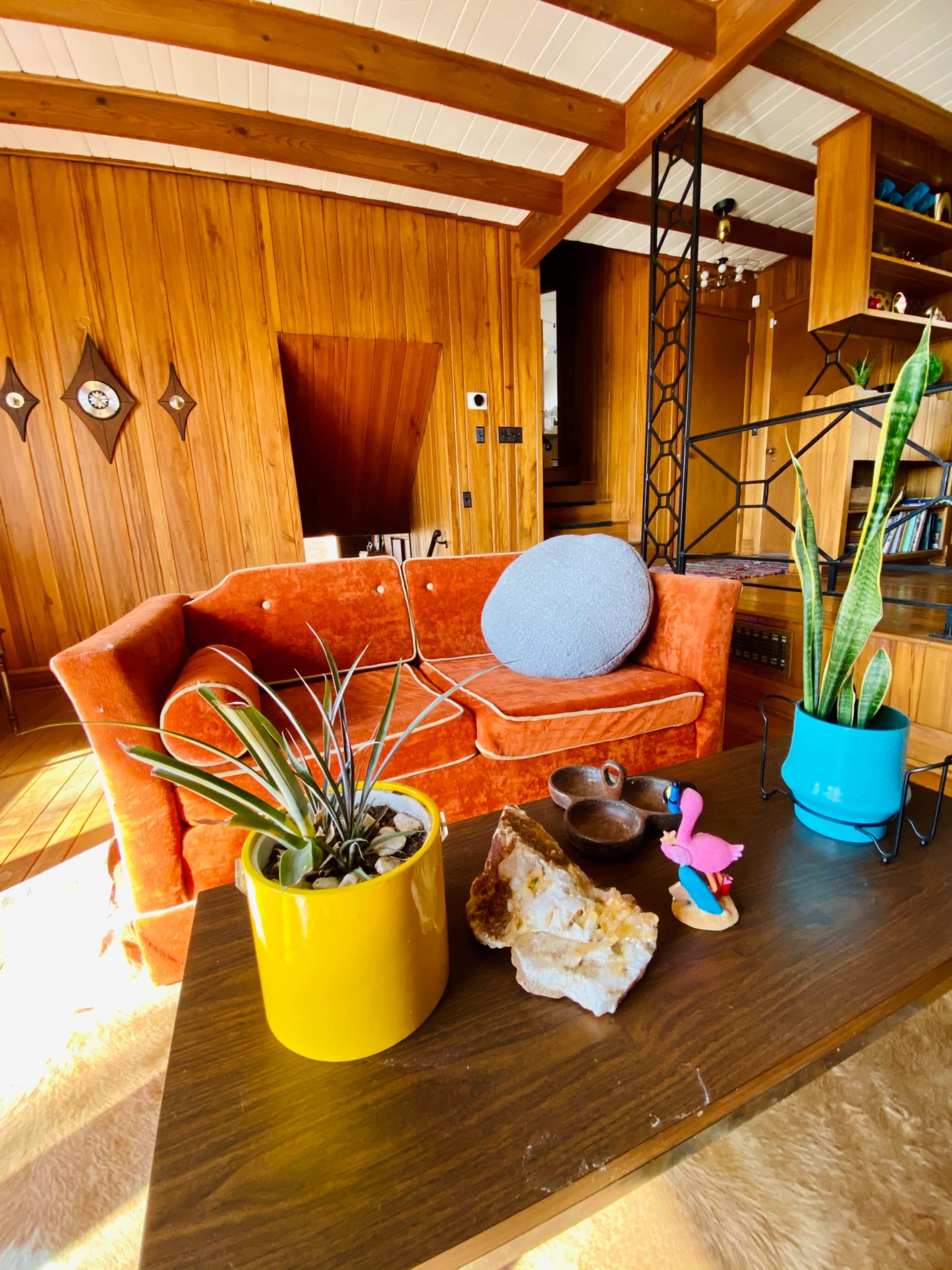 A living room with an orange couch, a wooden coffee table featuring decorative items, and a backdrop of wooden paneling and a staircase.