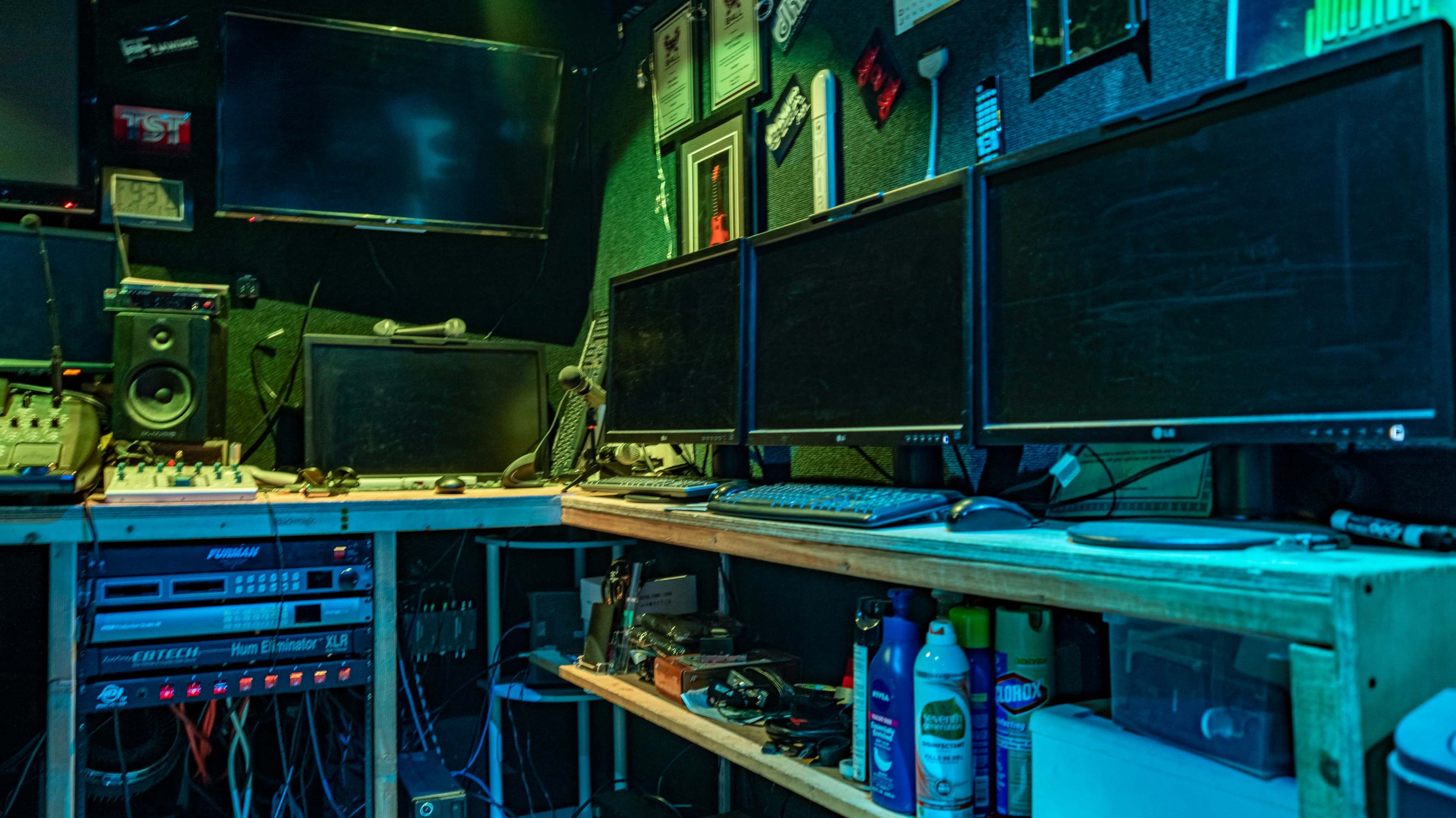 A workspace featuring multiple computer monitors, audio equipment, and various tools organized on wooden shelves.