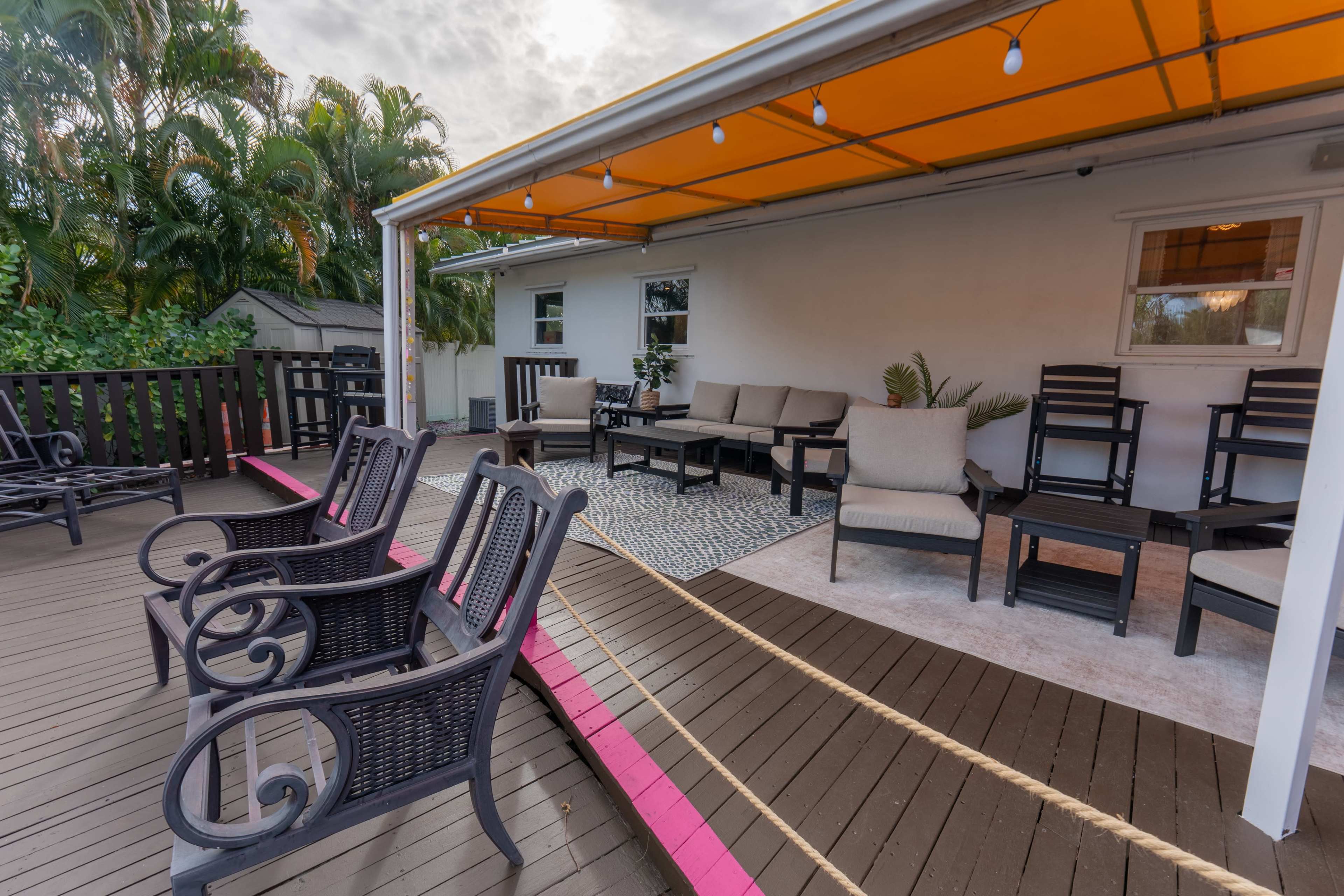 The image shows a covered outdoor patio area with seating arrangements, including lounge chairs and tables, under a bright yellow canopy.