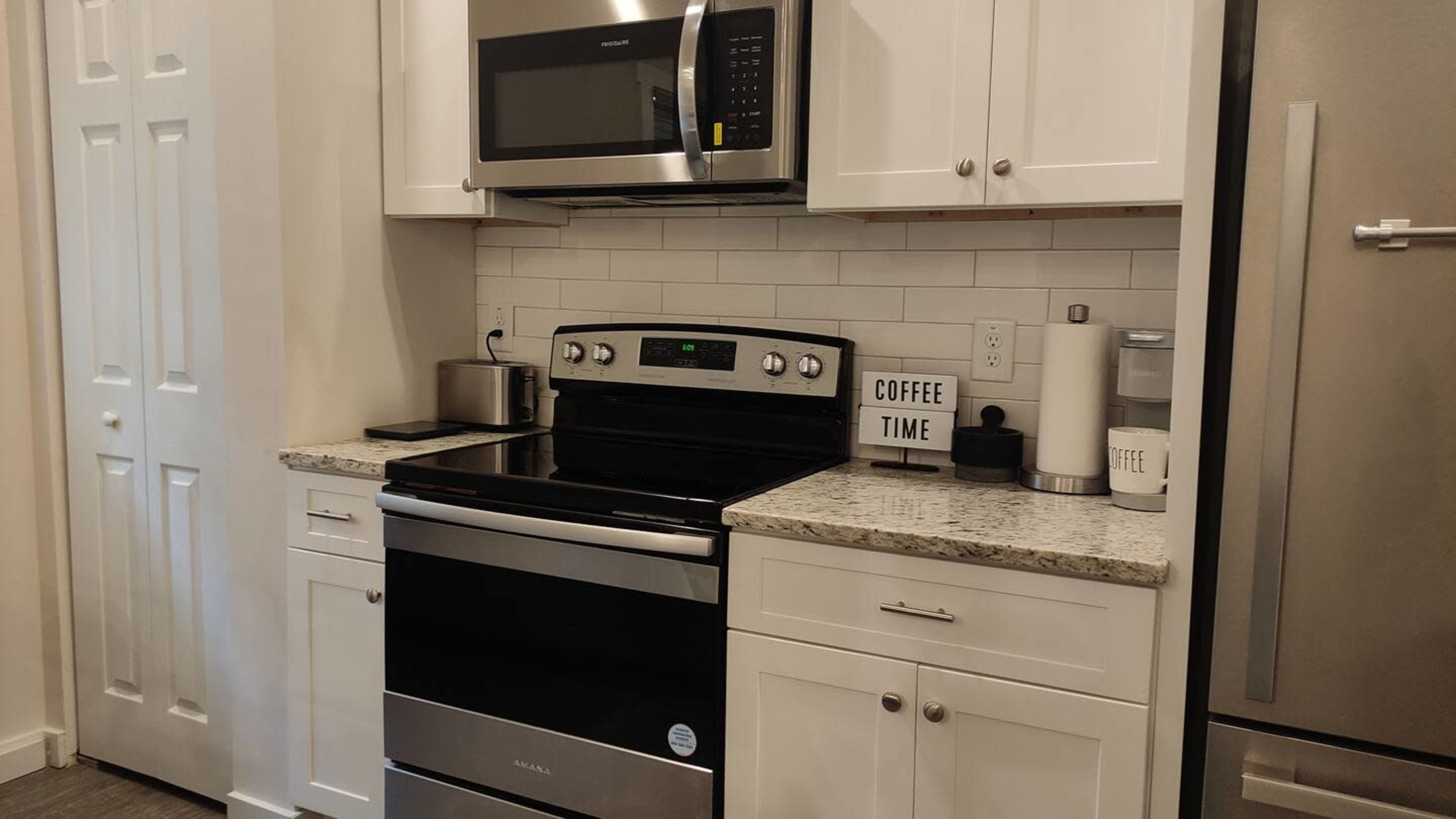 The image shows a kitchen with a stainless steel stove and microwave, white cabinets, and a countertop with a coffee-themed decoration.