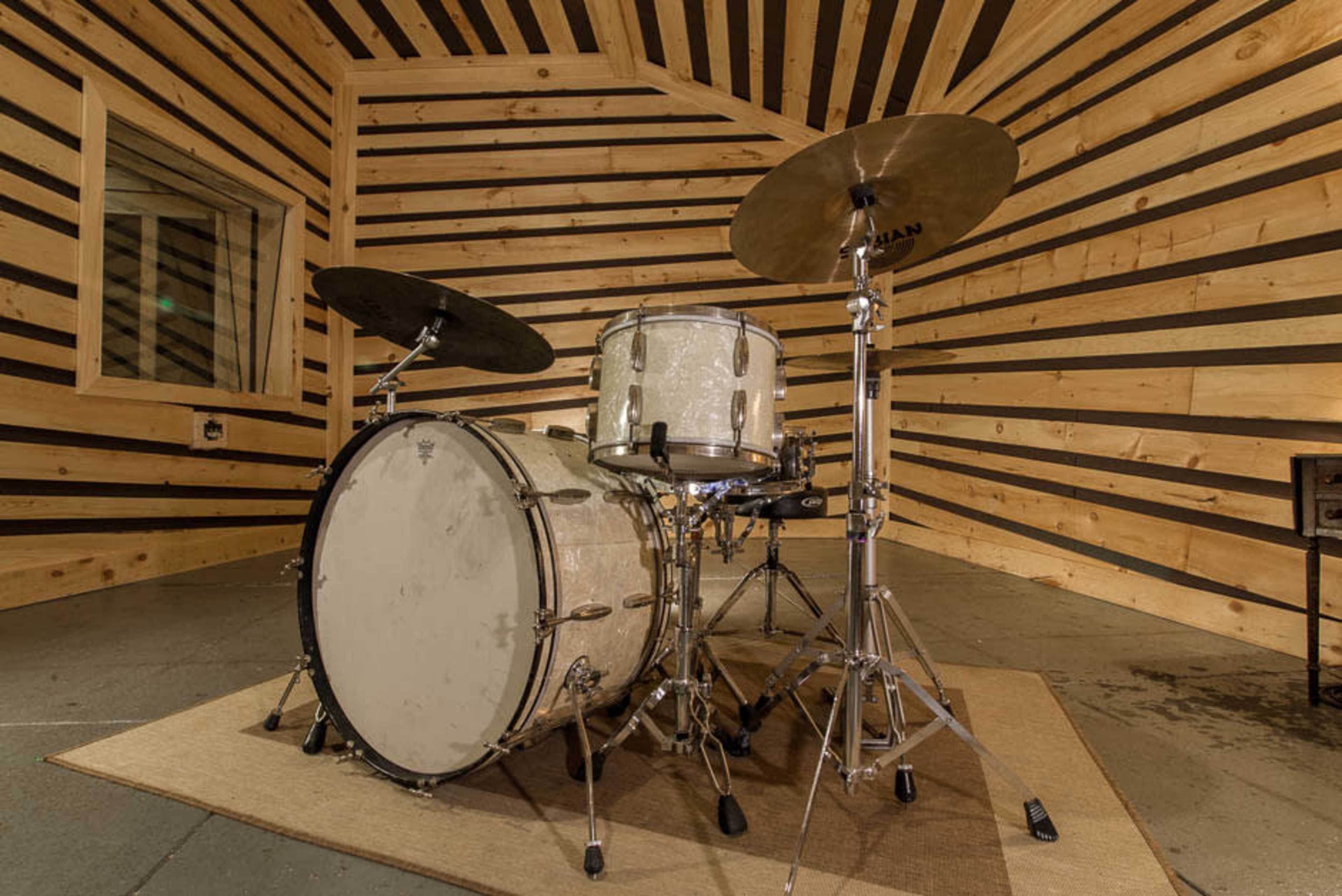 A drum set is positioned on a rug in a wooden room with horizontal black stripes on the walls.