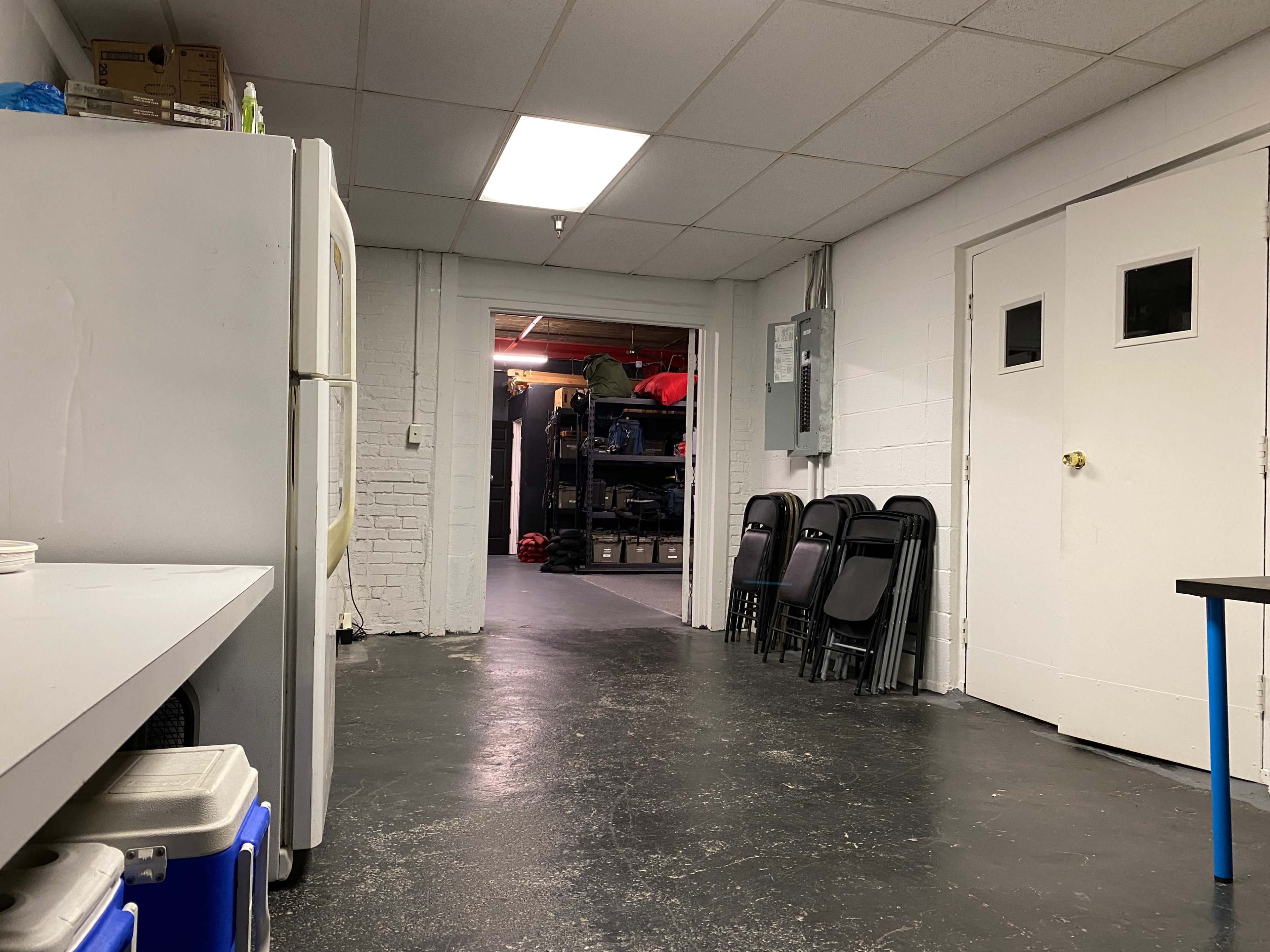 A long hallway leads to a storage area with stacked shelves and chairs lined up against the wall.