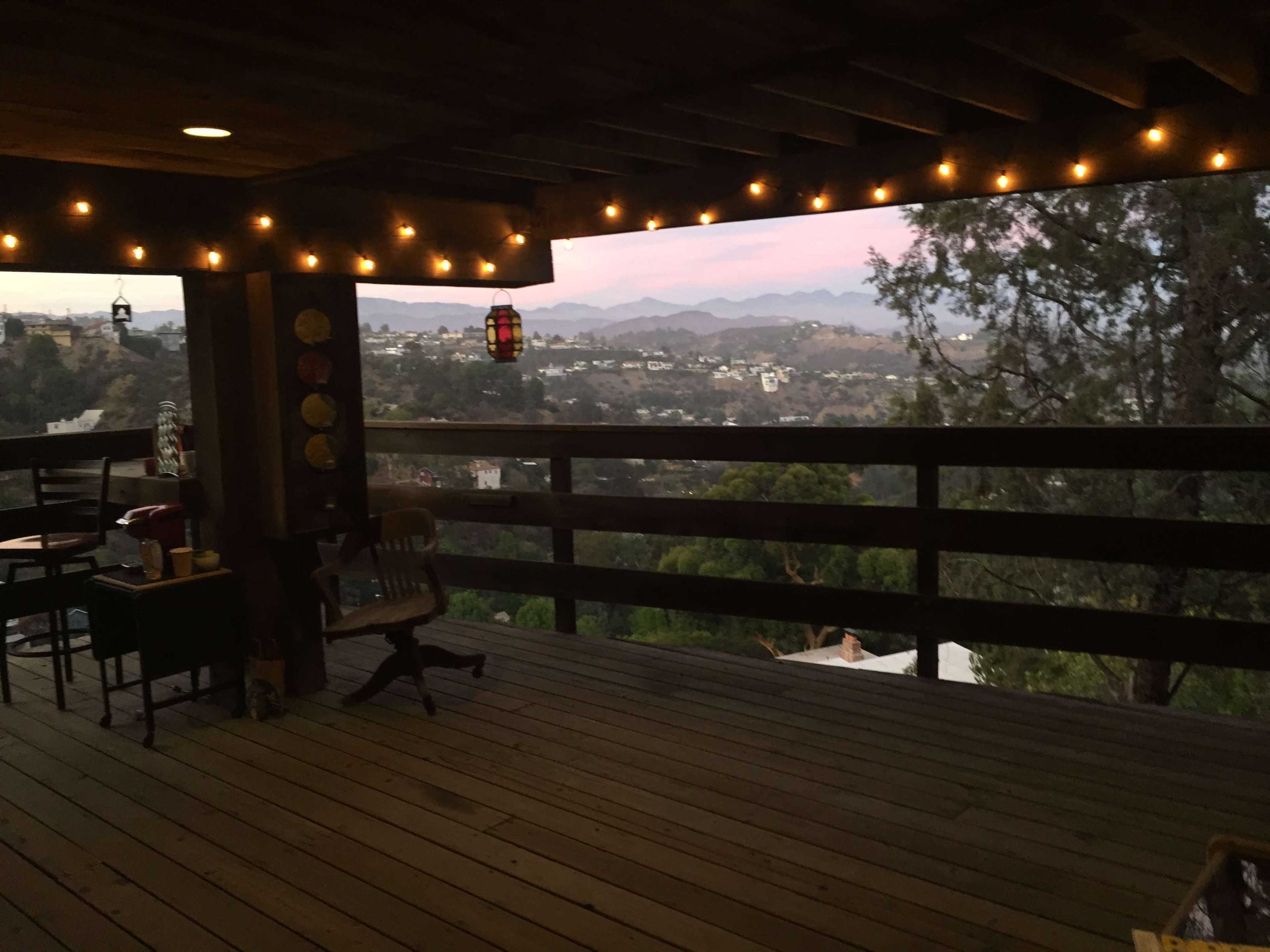 A wooden deck with string lights overlooks a mountainous landscape at dusk.