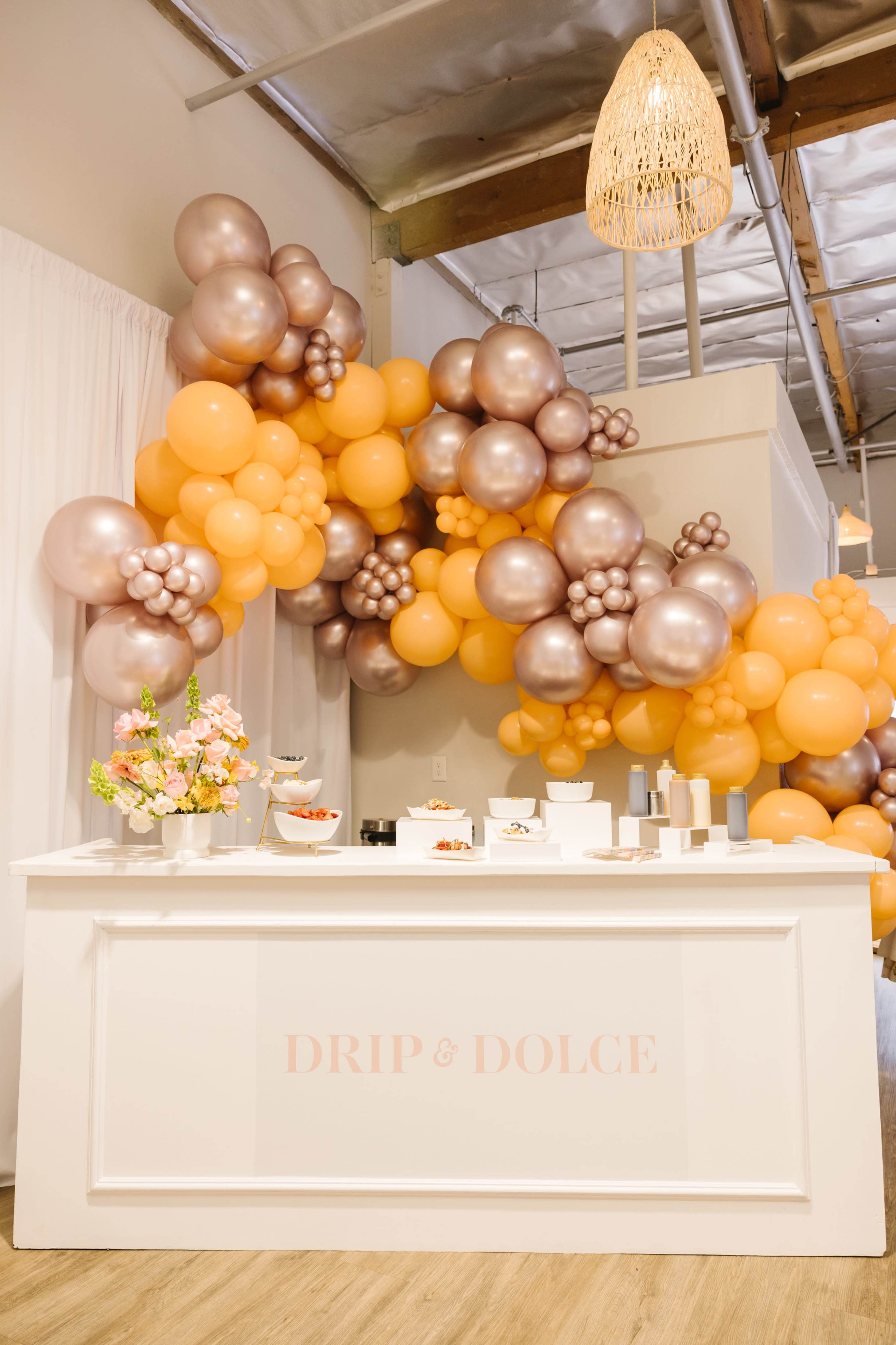 A decorated event space features a white reception counter adorned with pastel-colored balloons and floral arrangements.