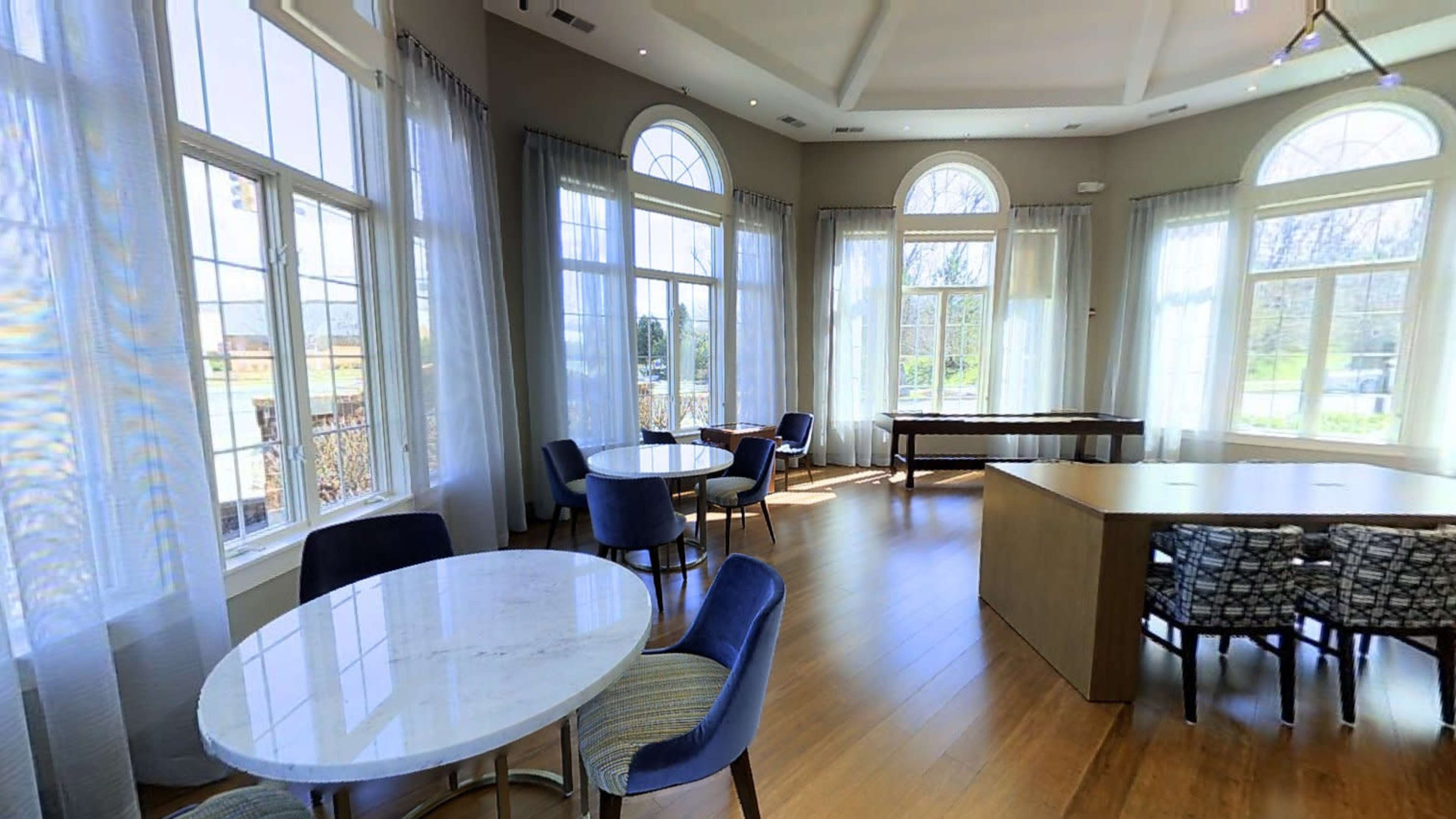 A bright, spacious interior with large windows, circular and rectangular tables, and chairs arranged around them.
