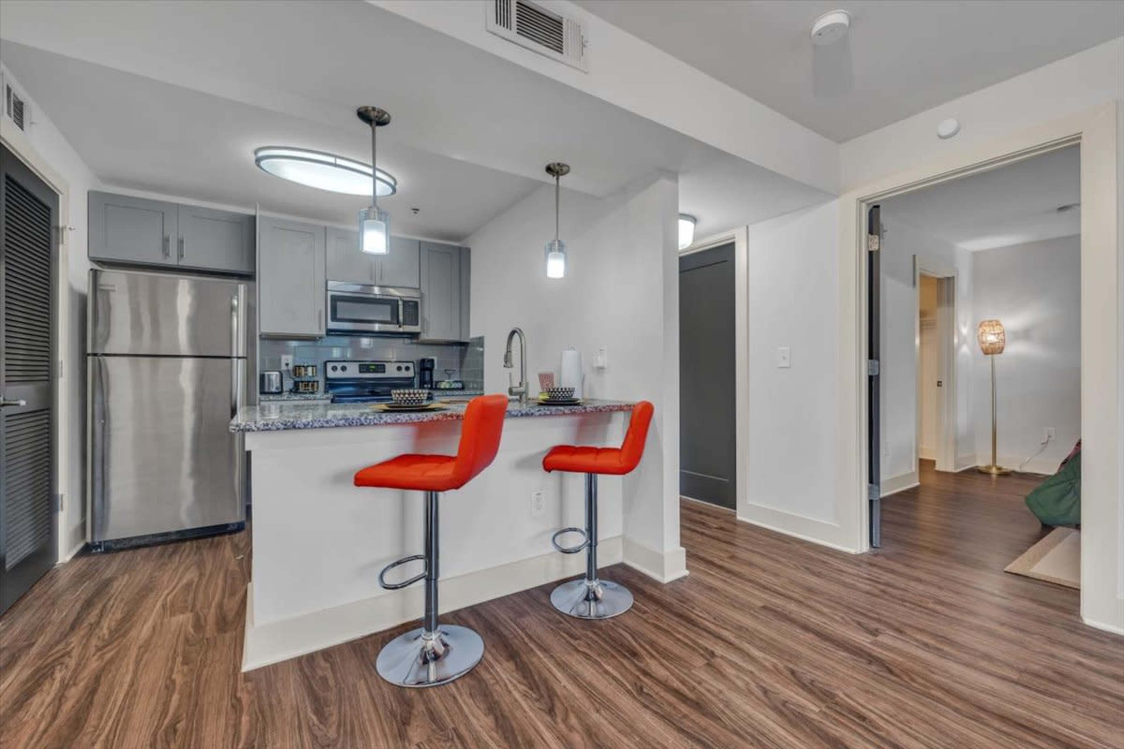 A modern kitchen area features a bar with two red stools, stainless steel appliances, and a granite countertop.