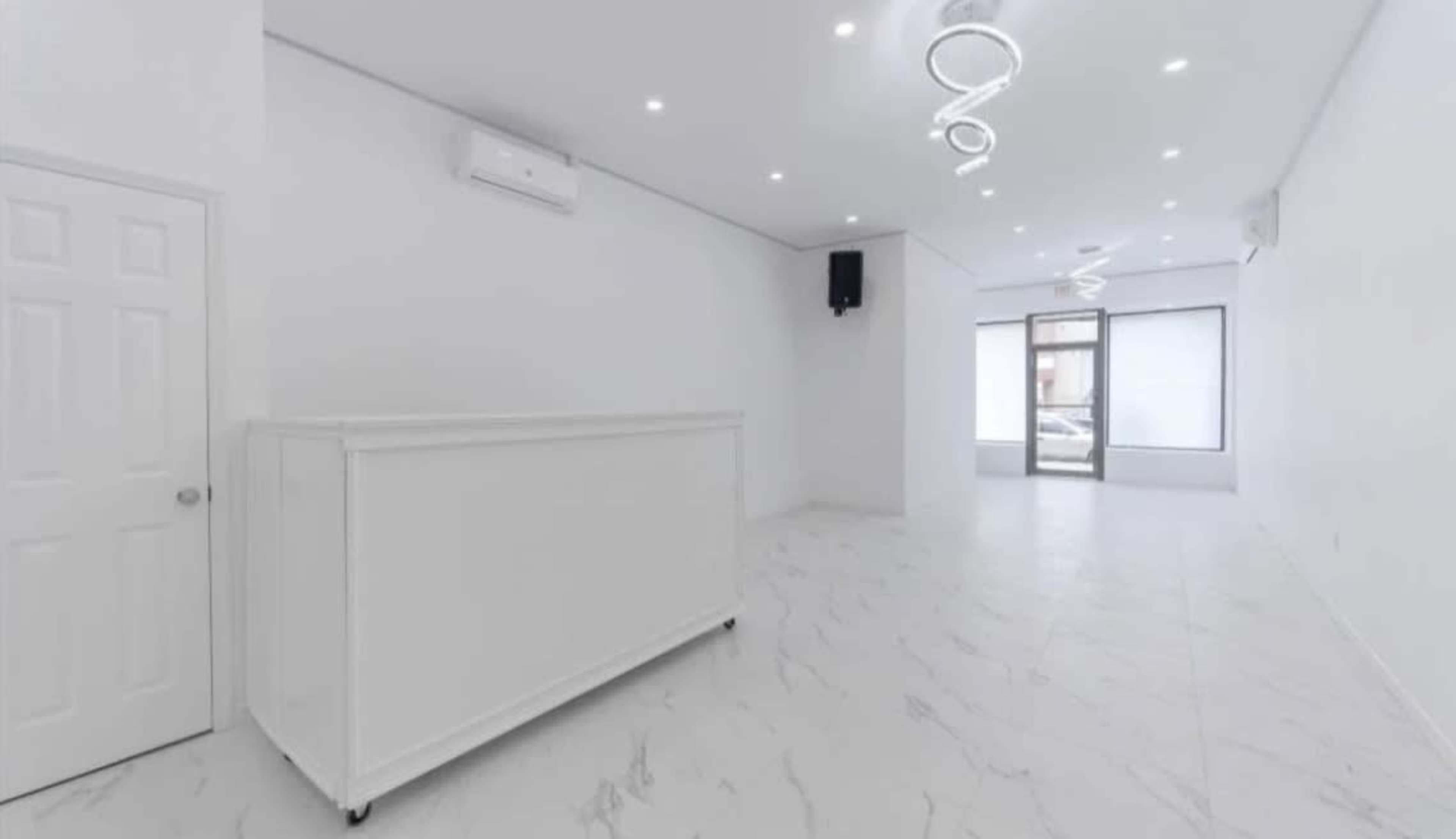 The image shows a spacious, empty room with white walls and a marble floor, featuring a front counter and large windows.