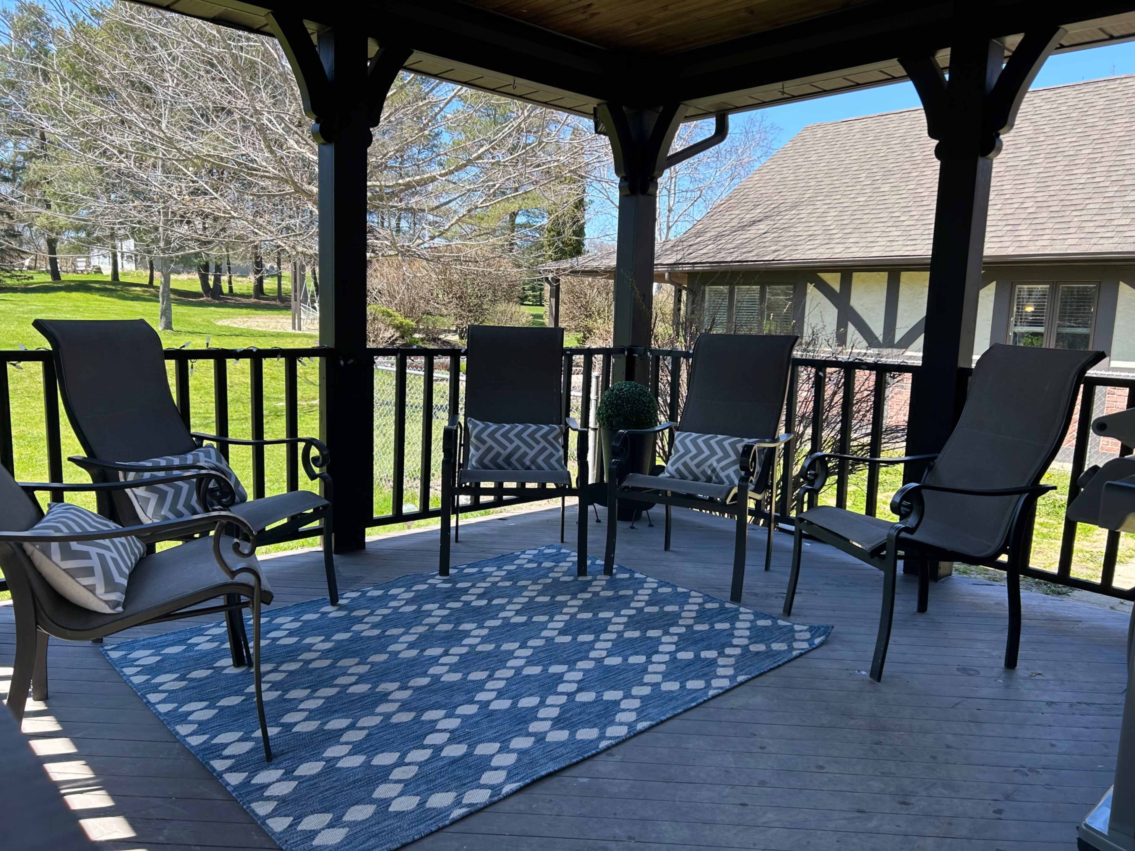 A covered outdoor porch featuring four chairs arranged around a blue patterned rug.