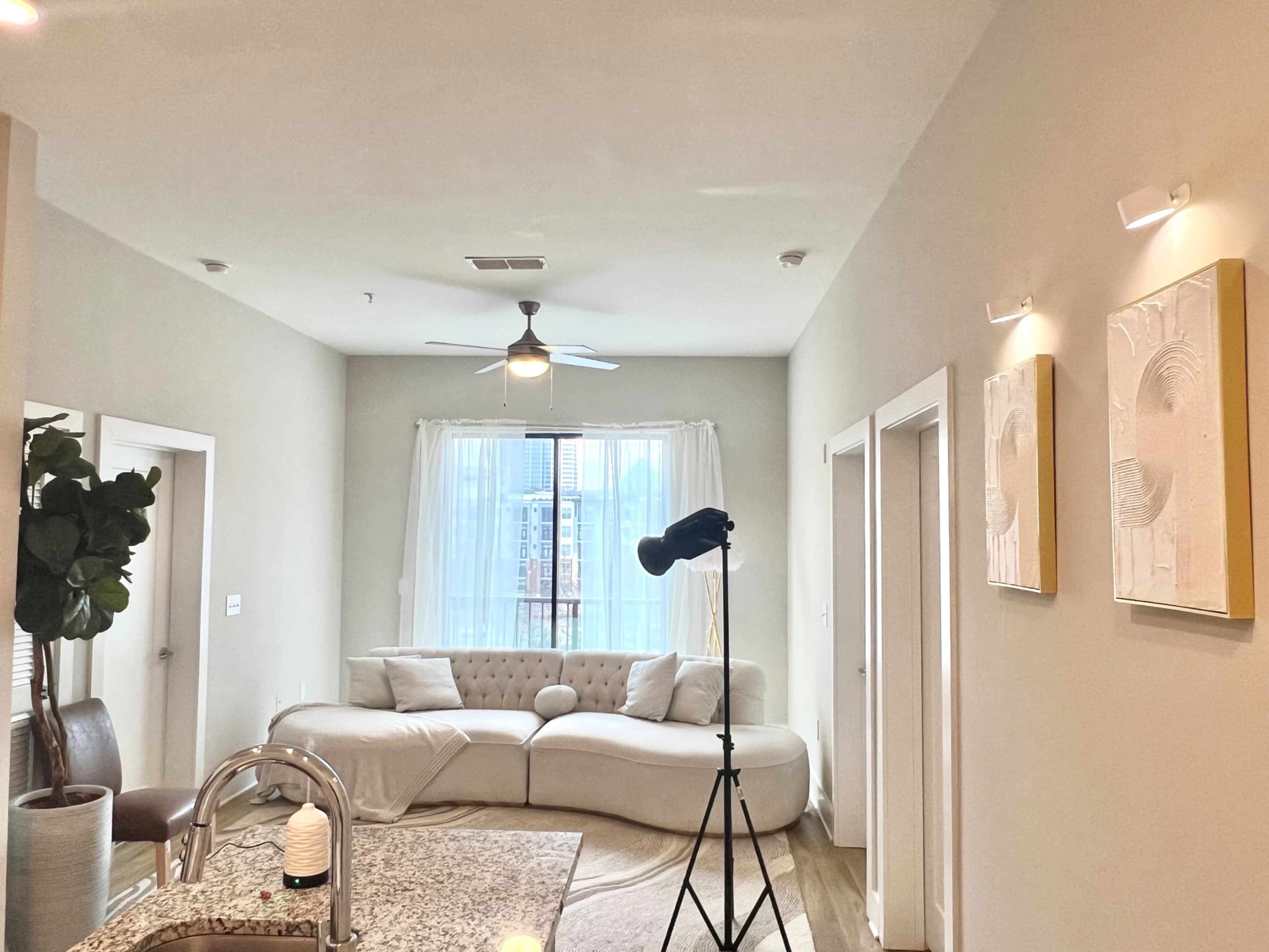 A modern living room with a curved sofa, a standing lamp, and two decorative wall pieces, all illuminated by natural light from a window.