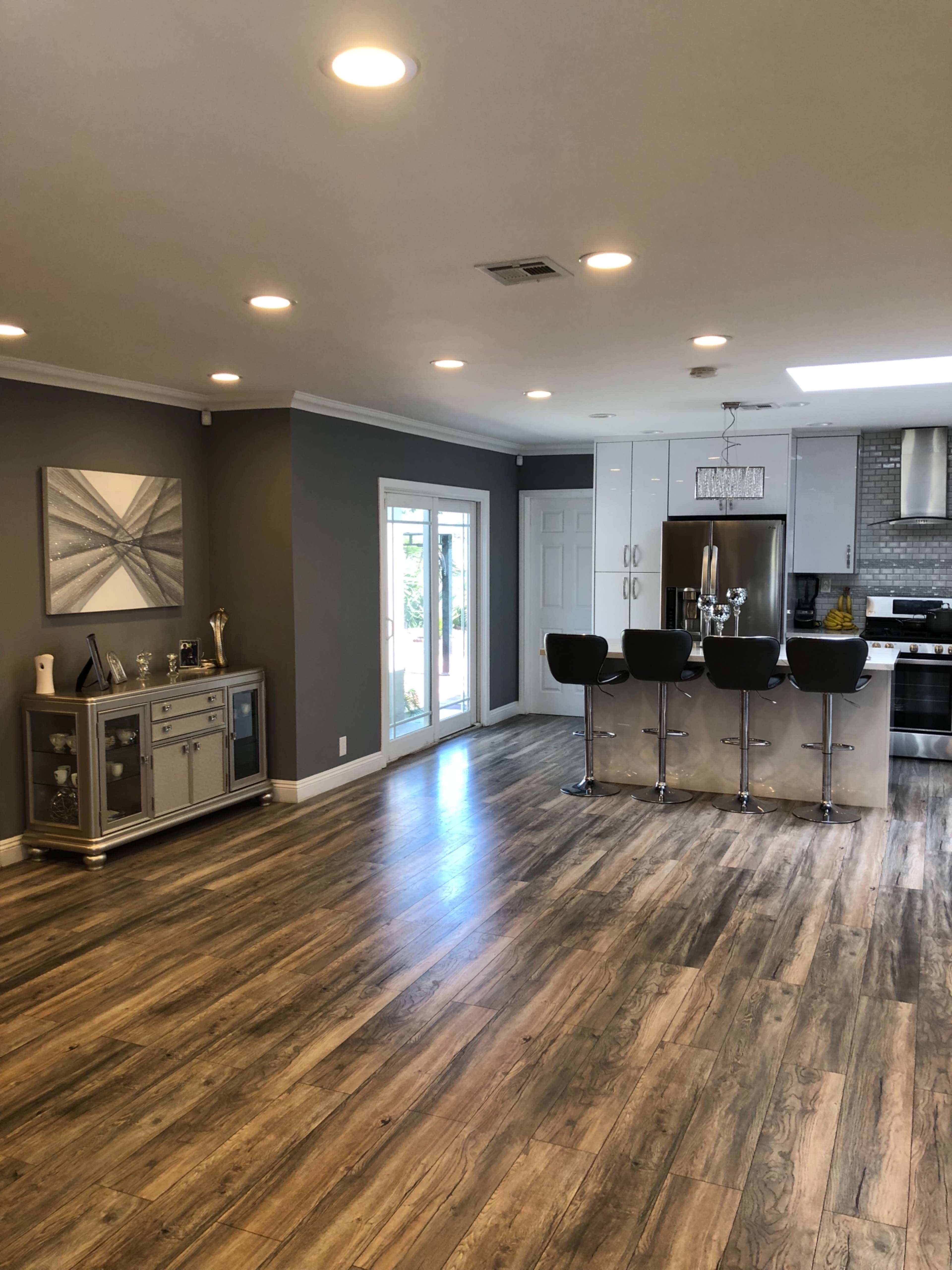 A modern kitchen and dining area features stainless steel appliances, a large island with bar stools, and large windows leading to an outdoor space.