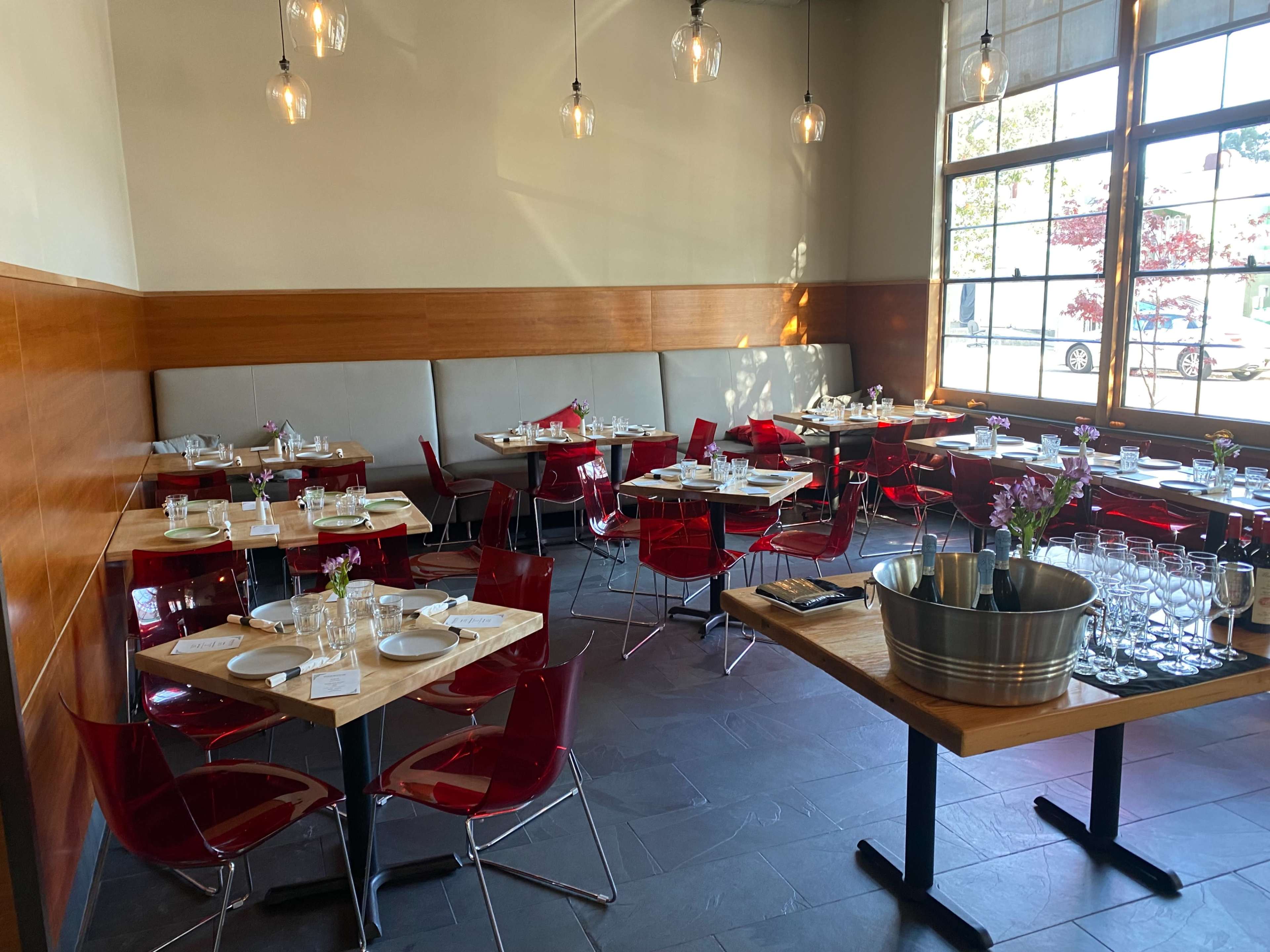 An indoor restaurant setting with red chairs and tables arranged neatly, featuring glassware and table settings on each table.