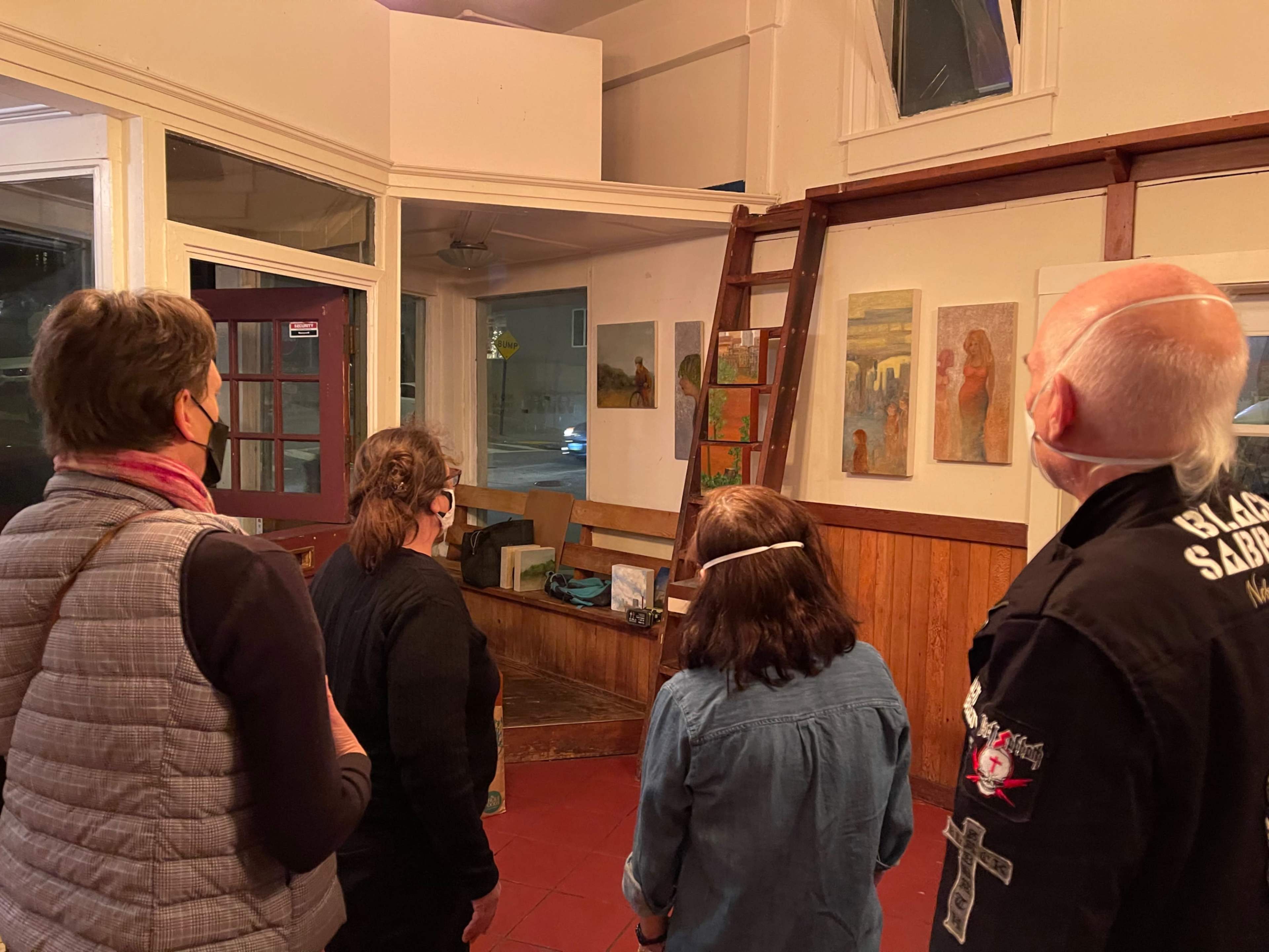 Four people observe artwork displayed on walls in a gallery setting.