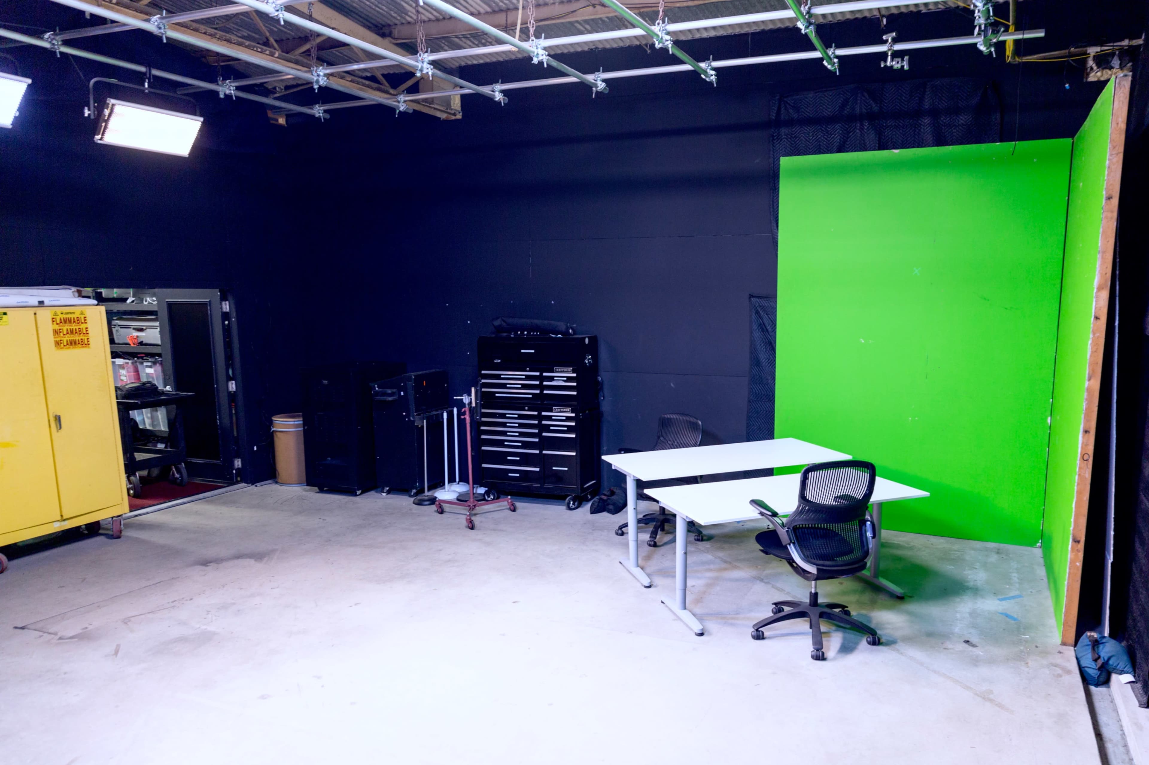 An empty studio space features a green backdrop, two tables, and various equipment on the side.
