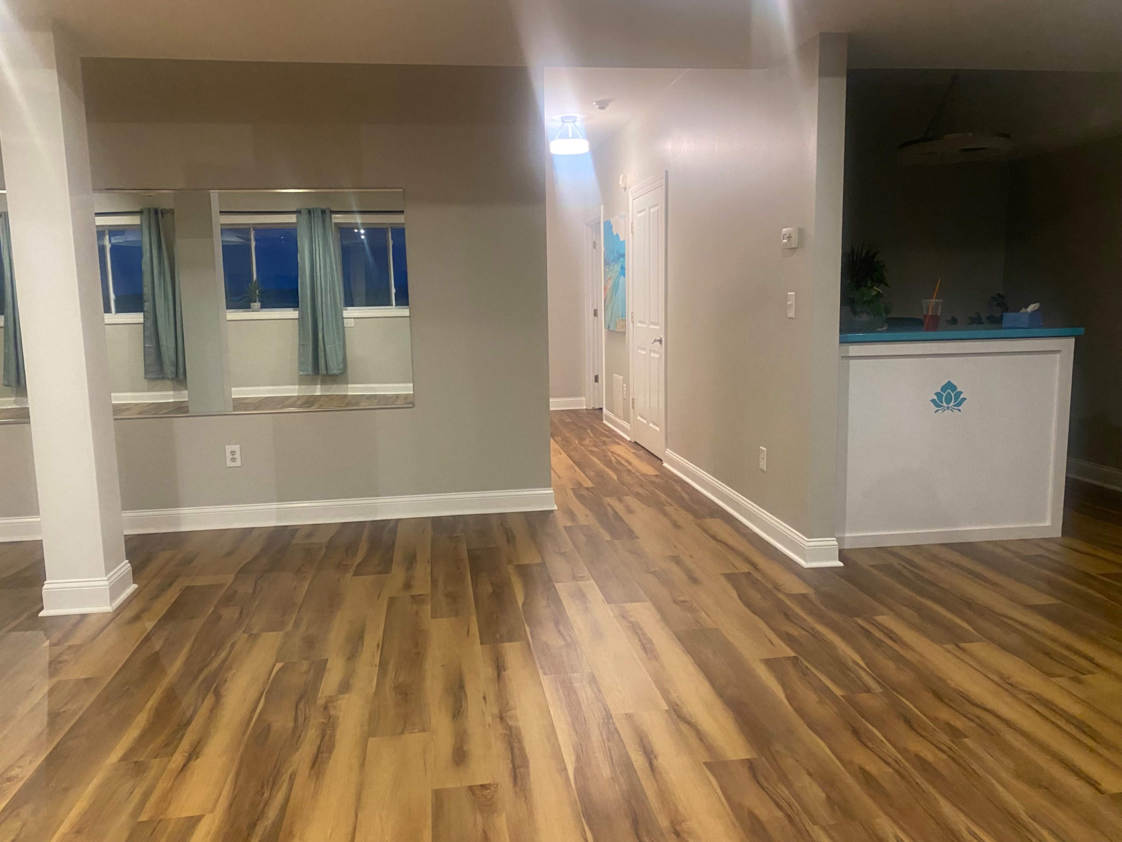 A well-lit interior space featuring wooden floors, a reception area with a counter, and large windows with curtains.